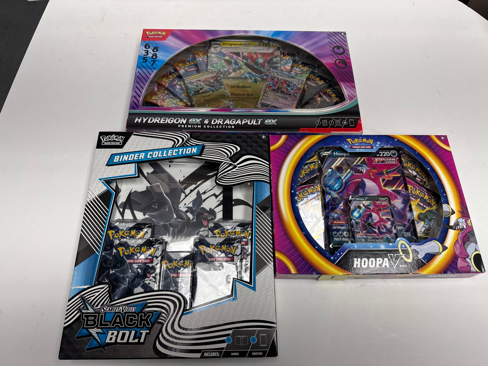 Pokemon TCG: Hydreigon & Dragapult EX Premium Collection, Scarlet & Violet Black Bolt Binder: This lot includes three Pokemon Trading Card Game (TCG) premium collections: the Hydreigon & Dragapult EX Premium Collection, the Scarlet & Violet - Black Bolt Binder Collection, and the Hoopa V Box. 