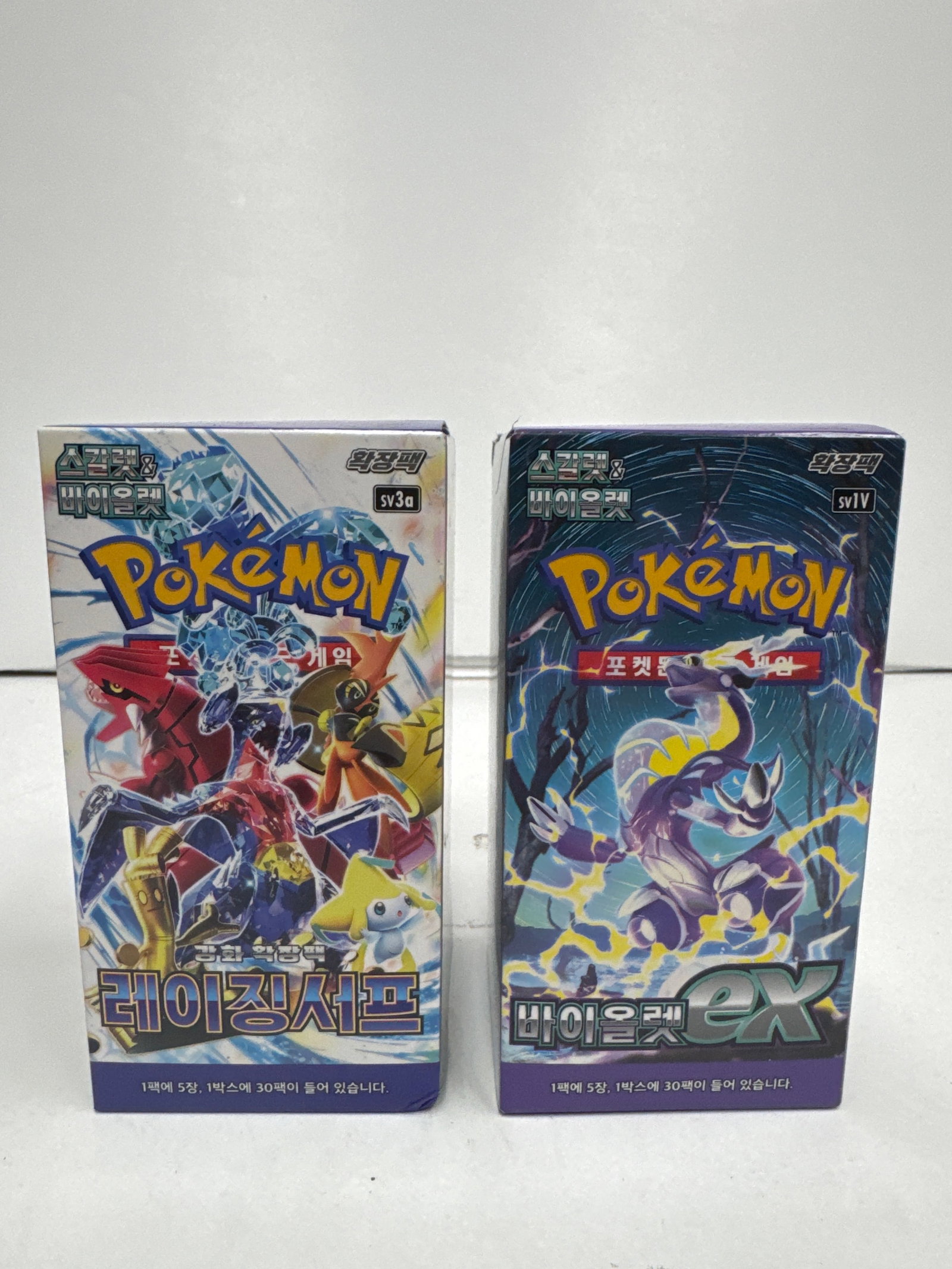 Two Pokemon Trading Card Game Booster Boxes: SV3a & SV1v: This lot includes two Pokemon Trading Card Game booster boxes. The first is labeled SV3a and features various Pokemon in a dynamic battle scene. The second is labeled SV1v and showcases a purple, drag