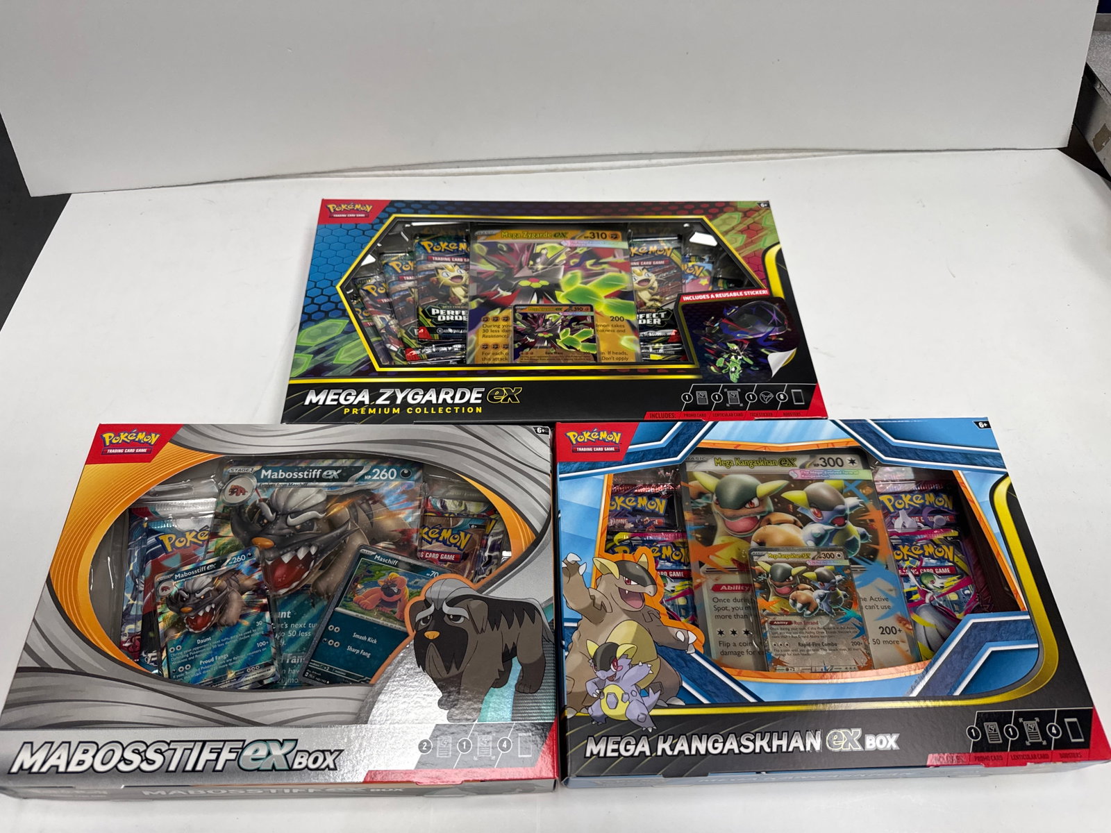 Pokemon TCG Mega Zygarde EX, Mega Kangaskhan EX, and Mabosstiff EX Premium Collections: This lot includes three Pokemon Trading Card Game Premium Collections: Mega Zygarde EX, Mabosstiff EX, and Mega Kangaskhan EX. Each box contains booster packs, promo cards, and other collectibles, off