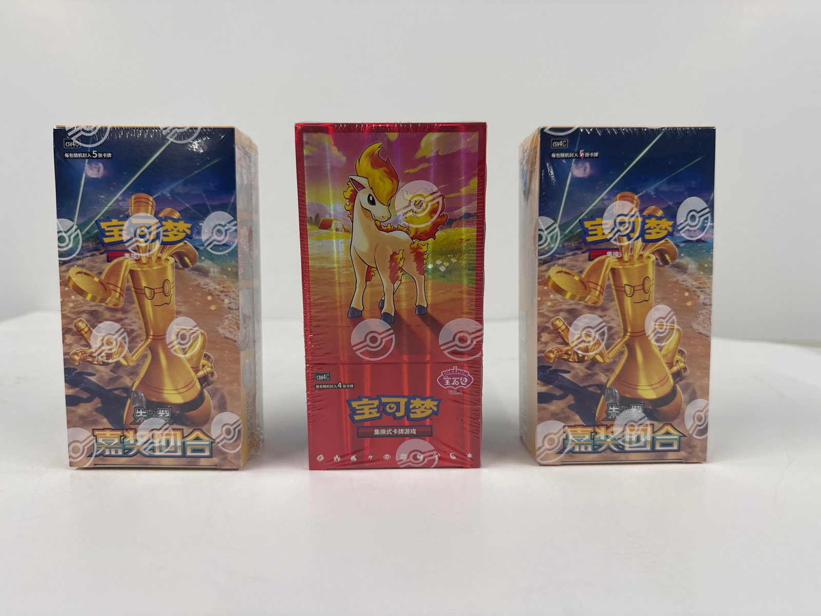 Three Booster Boxes of Pokemon Trading Card Game: Three sealed booster boxes of the Pokemon Trading Card Game. The boxes feature vibrant artwork with characters and creatures from the Pokemon universe. The central box is red with a depiction of Ponyt