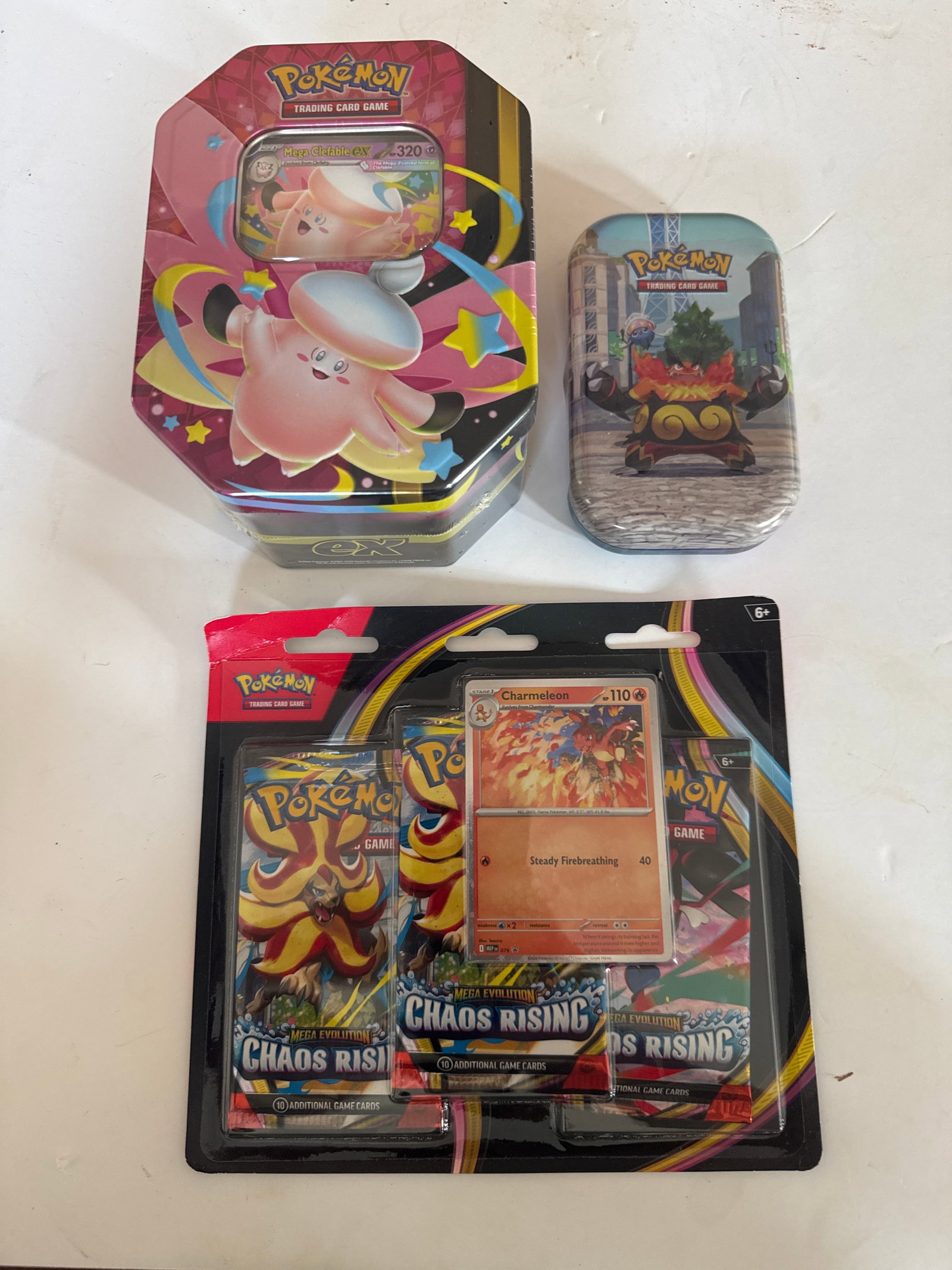 Pokemon Trading Card Game Tins and Booster Pack Collection: This lot includes two Pokemon Trading Card Game tins and one booster pack collection. The tins feature artwork of Pokemon characters and game elements. One is a mini tin. The booster pack collect