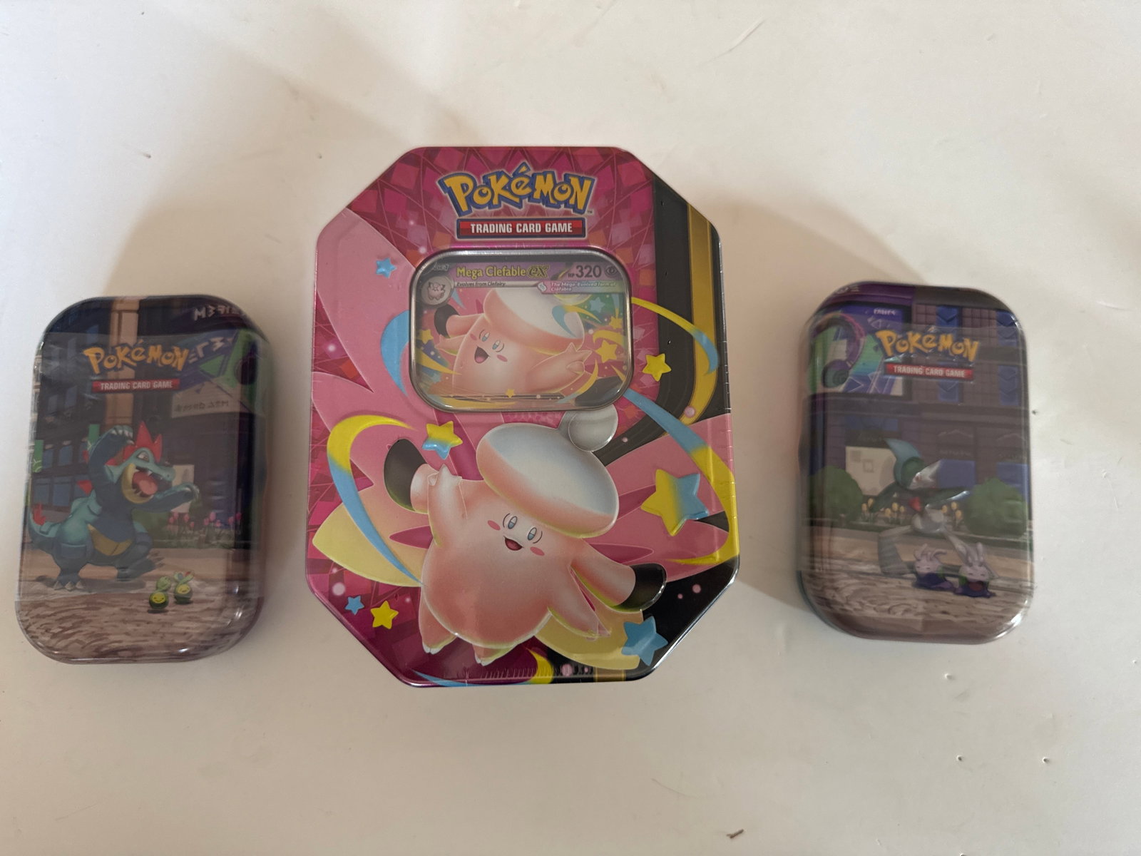 Pokemon Trading Card Game Tins - Mega Clefable EX, Feraligatr, and Gallade: This lot includes three Pokemon Trading Card Game tins. The central tin features Mega Clefable EX and has an octagonal shape. The two smaller tins feature Feraligatr and Gallade respectively.