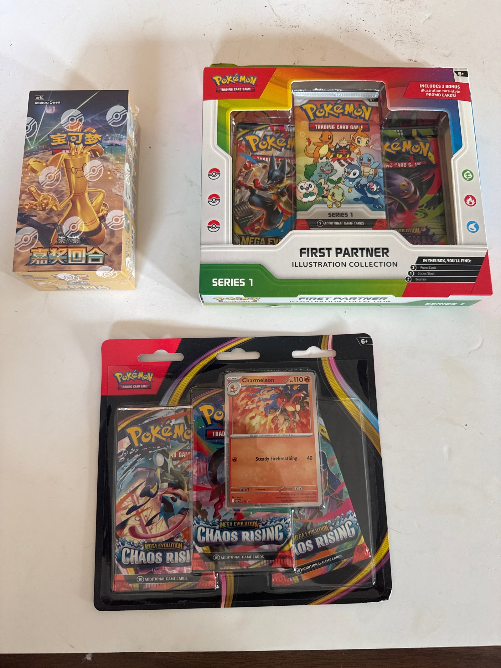 Pokemon Trading Card Game Collection: First Partner Illustration Collection & Chaos Rising Booster: This lot includes a Pokemon TCG First Partner Illustration Collection Series 1 box, featuring 3 booster packs and 3 promo cards. Also included is a Pokemon TCG Mega Evolution Chaos Rising blister pack
