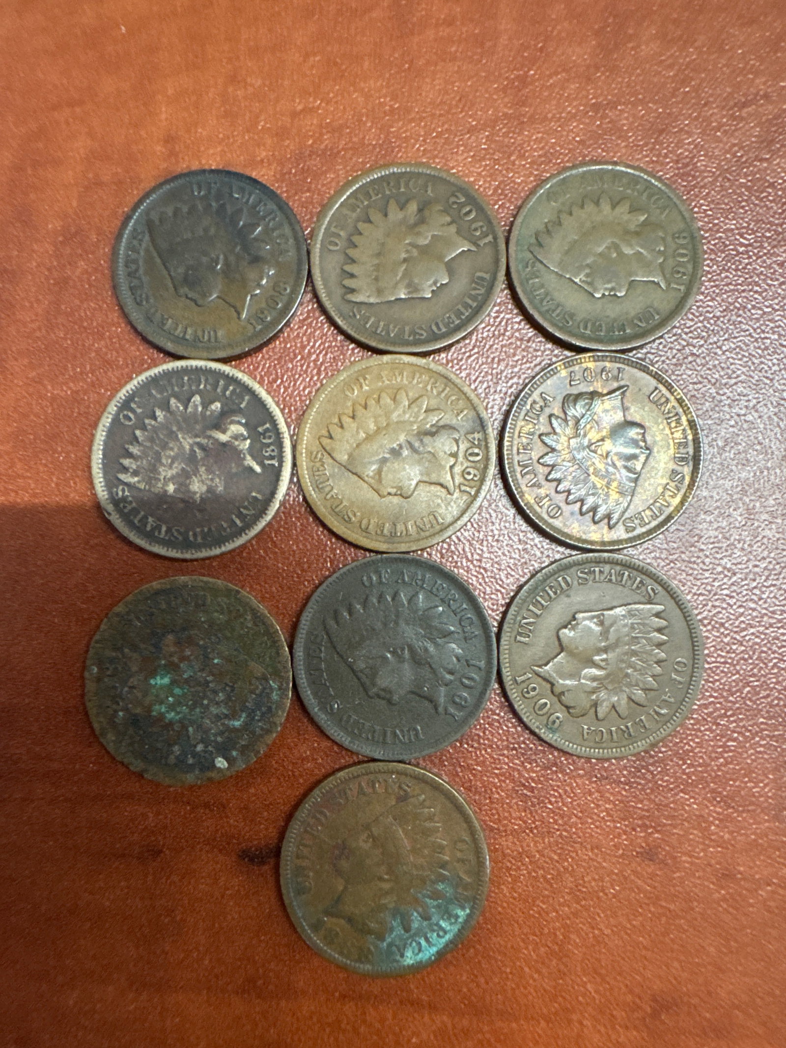 Collection of Indian Head Pennies: A collection of nine Indian Head pennies, featuring various dates including 1906, 1907, and 1908. The coins show signs of wear and some oxidation, consistent with their age.
