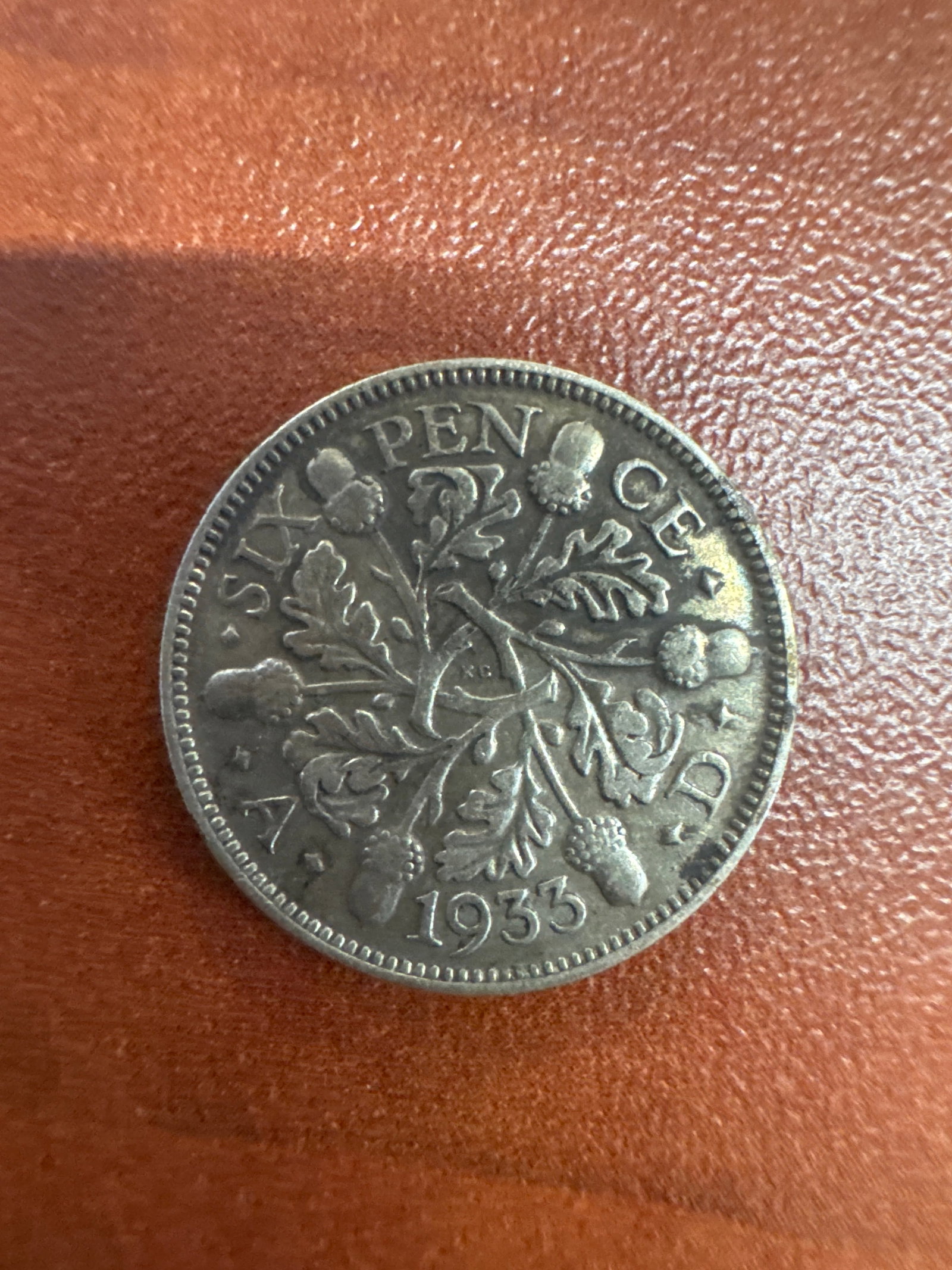 1933 British Sixpence Coin: A silver British sixpence coin from 1933, featuring King George V on the obverse and a floral design with acorns on the reverse.