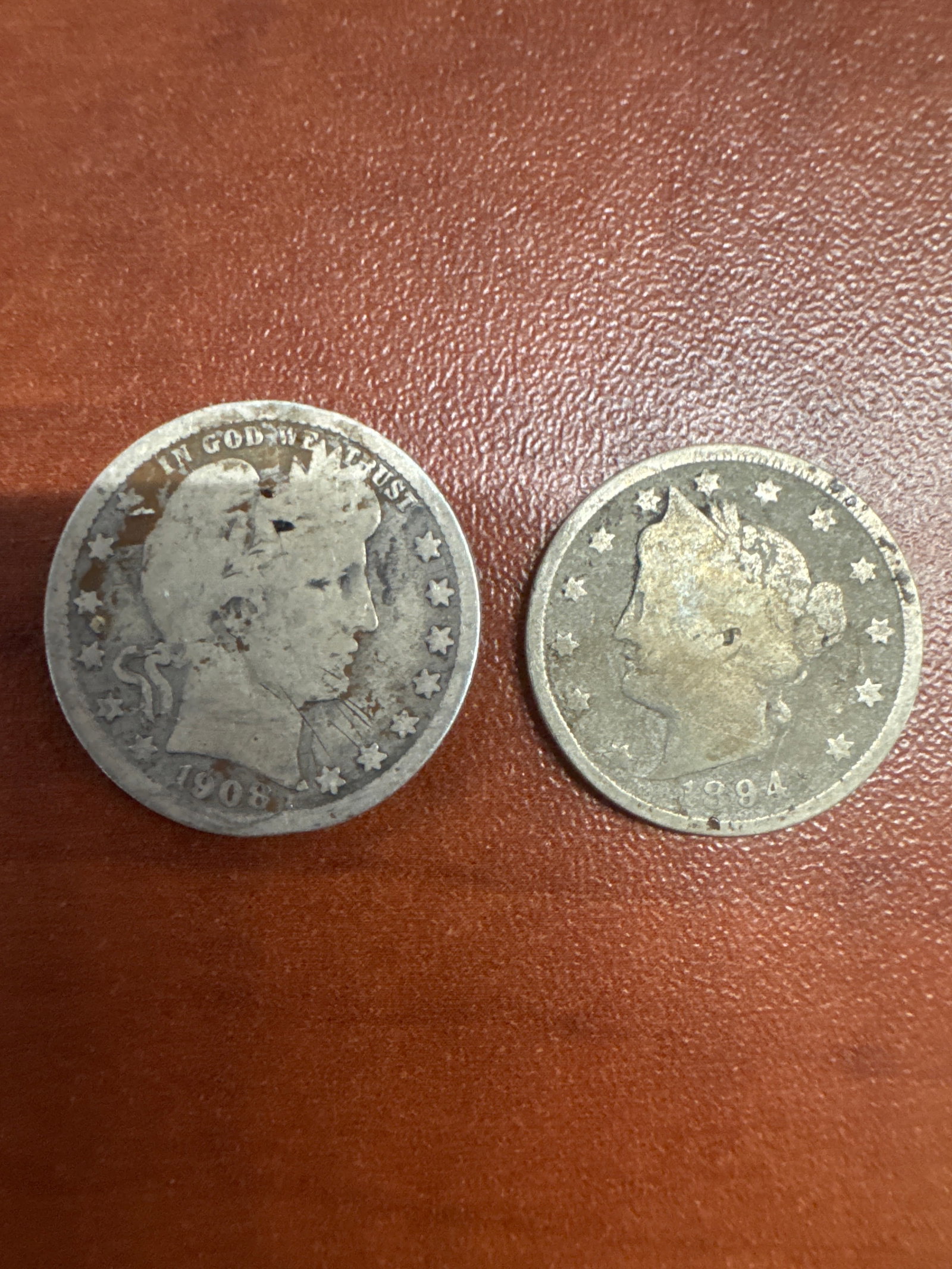 Two US Silver Quarters: 1908 Barber Quarter and 1894 Liberty Head Quarter: This lot features two United States silver quarters. The first is a 1908 Barber quarter, identifiable by its obverse portrait of Lady Liberty and reverse depiction of an eagle. The second is an 1894 L