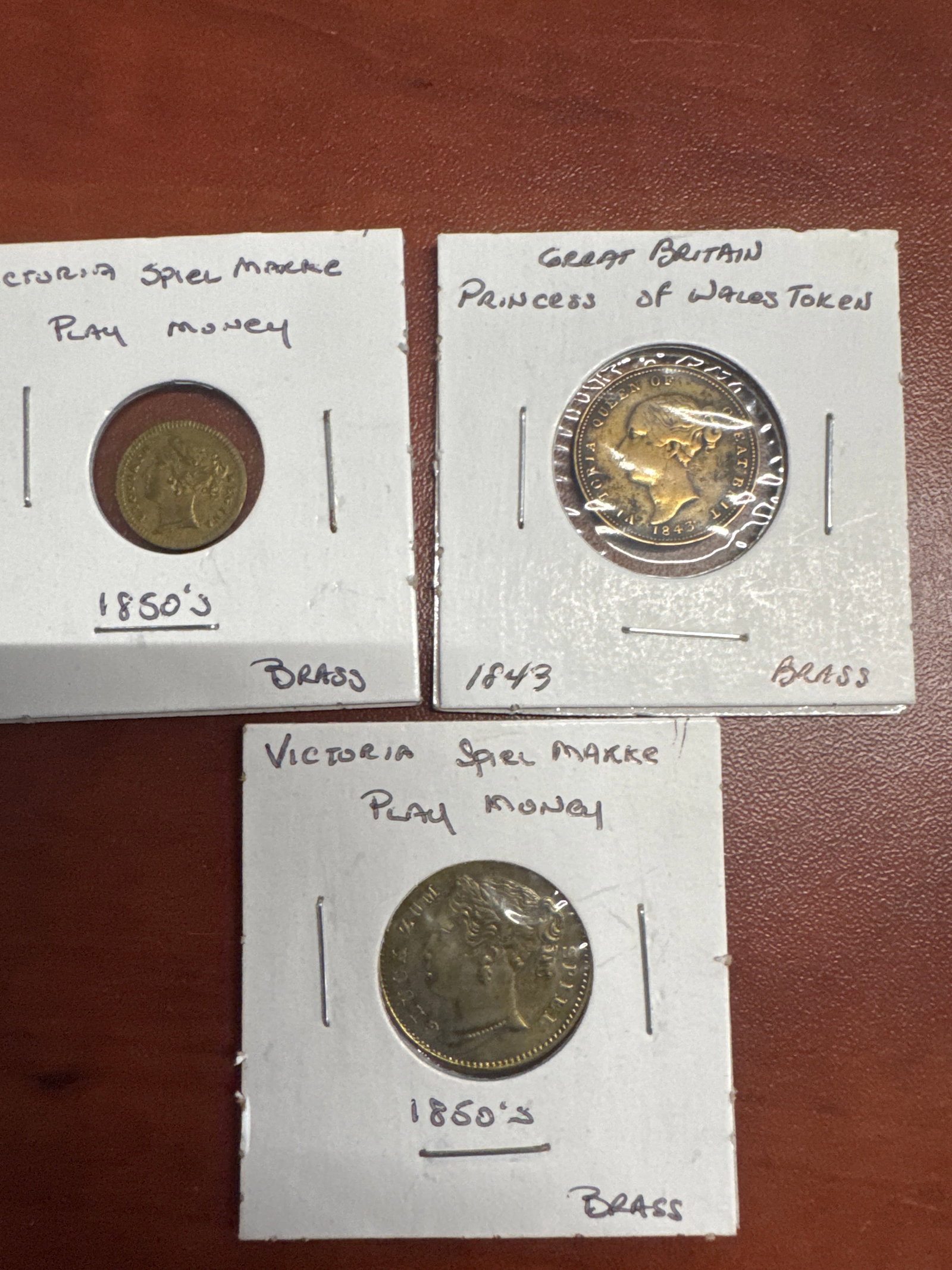 Collection of Three Victorian Era Tokens: This lot features three brass tokens from the Victorian era. Two tokens are labeled 'Victoria Spiel Marke Play Money' and dated 1850s. The third token is from Great Britain, identified as a &#