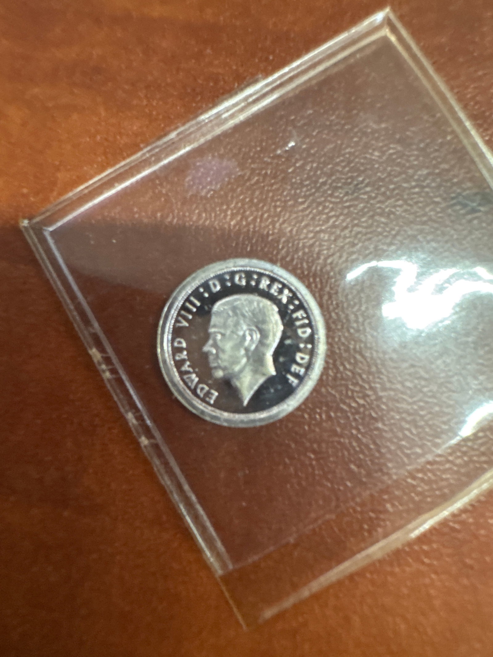 1936 Edward VIII Silver Two Pence Coin: A silver two pence coin from 1936 featuring a profile of King Edward VIII on the obverse and the numeral '2' surrounded by a wreath on the reverse. The coin is encapsulated in protective plast
