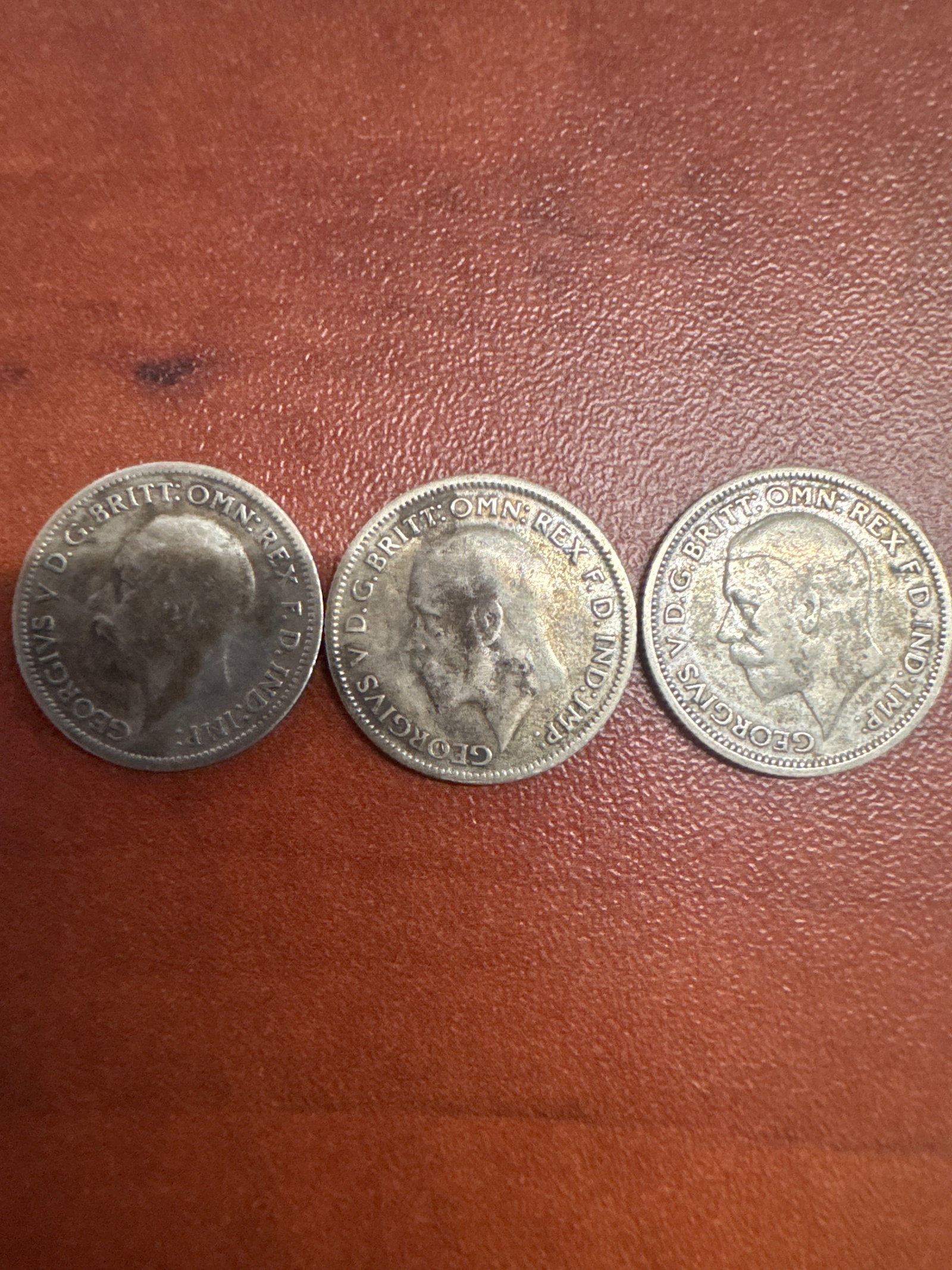 Three British Silver Sixpence Coins - George V: A collection of three British silver sixpence coins featuring King George V. The coins display the profile of the King on one side and intricate floral designs on the other. Dates visible include 1928