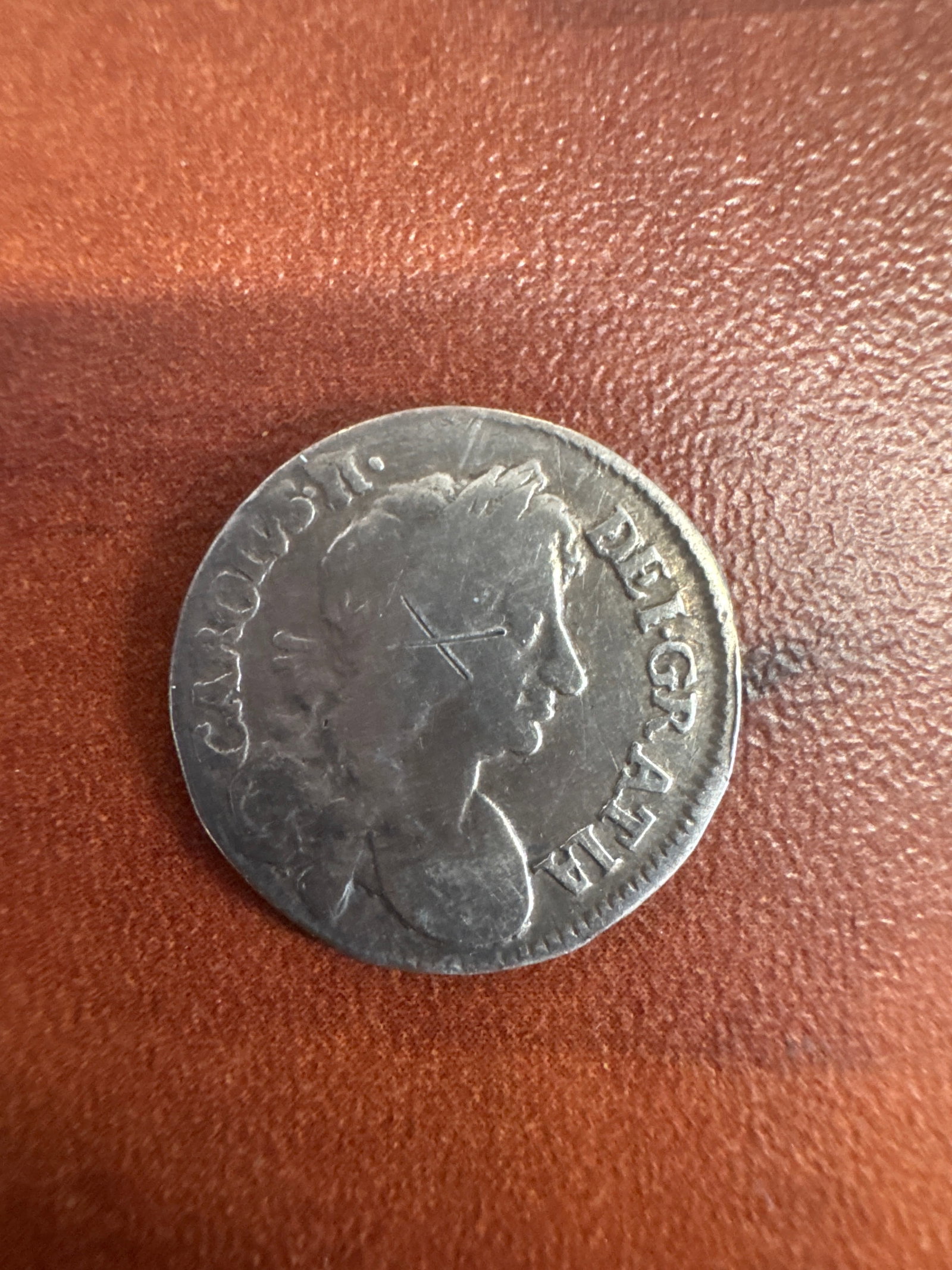 Silver Coin with Profile of Monarch and Crowned Emblem: A silver coin featuring a profile of a monarch on one side, with the inscription 'CAROLVS II DEI GRATIA' and a cross-like mark. The reverse side displays a crowned emblem with floral
