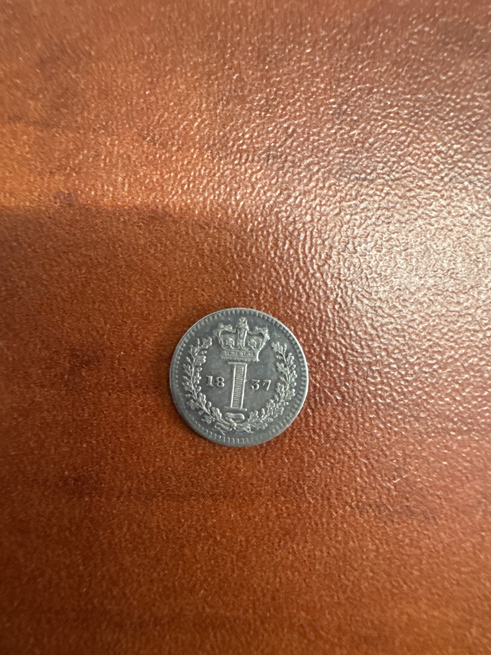 1837 British Silver Coin - 1 Penny: A 1 Penny silver coin from 1837, featuring a portrait of a monarch on one side and a crown and denomination on the other.