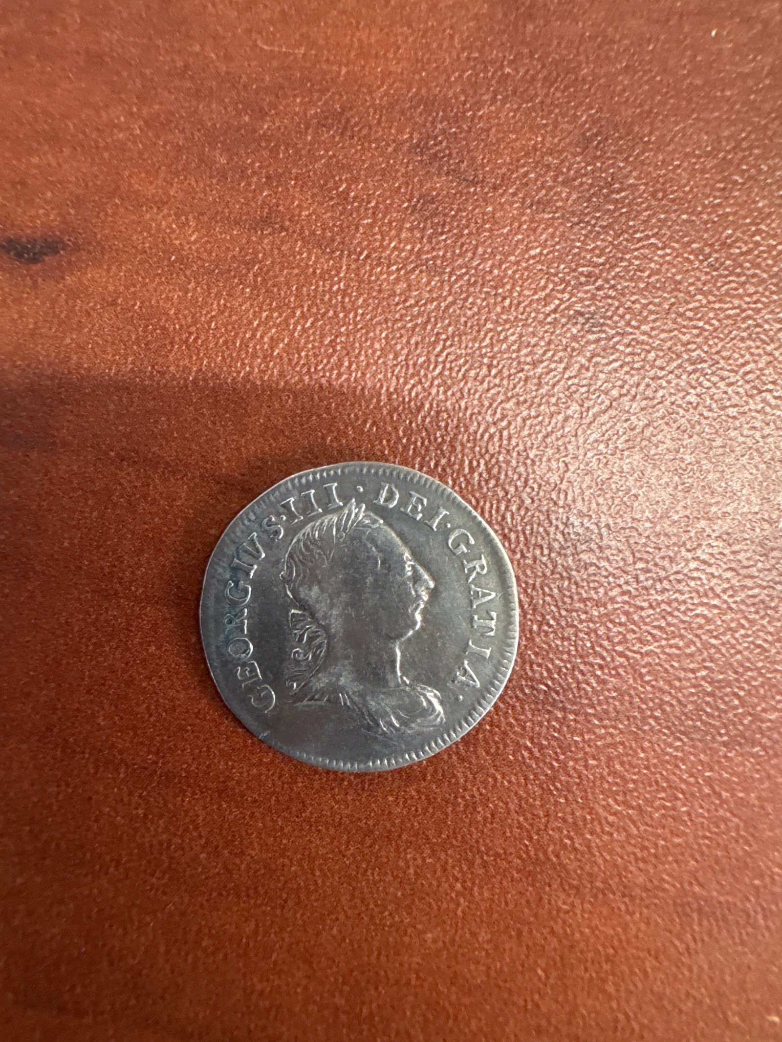 George III Silver 4 Pence Coin: A George III silver 4 pence coin, featuring a profile portrait of the King on the obverse and the numeral '4' crowned on the reverse. The coin shows signs of wear consistent with