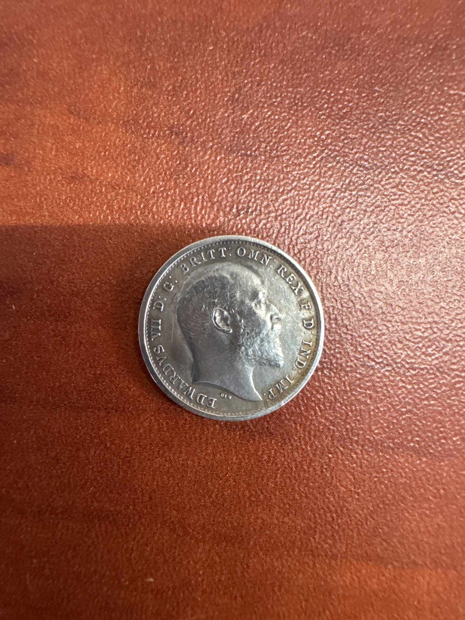 1902 United Kingdom Edward VII 4 Pence Silver Coin: A silver 4 pence coin from the United Kingdom, dated 1902, featuring a portrait of King Edward VII on the obverse and a crown with the numeral '4' surrounded by a wreath on the reverse. 