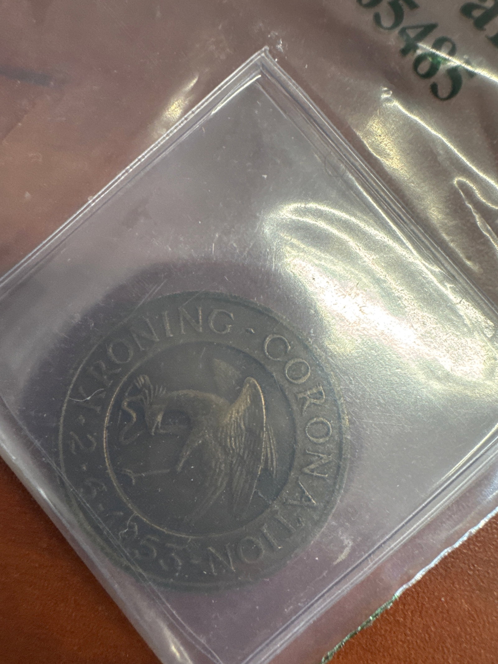1953 2 Kronor Coin - Queen Elizabeth II: A 1953 two Kronor coin featuring Queen Elizabeth II on the obverse and a crowned eagle on the reverse. The coin appears to be made of a bronze alloy and is housed in a protective plastic sleeve.