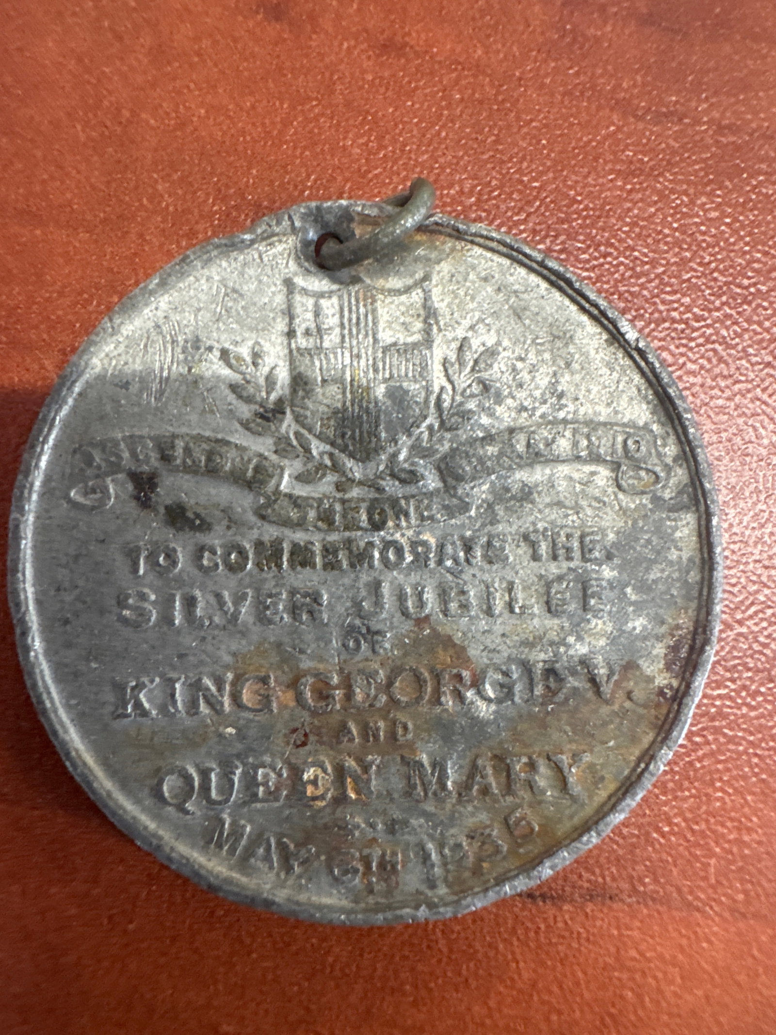 Commemorative Medal for King George V and Queen Mary's Silver Jubilee, May 1935: A circular medal commemorating the Silver Jubilee of King George V and Queen Mary, dated May 1935. The obverse features a heraldic crest and a banner with the inscription "TO COMMEMORATE THE SILV