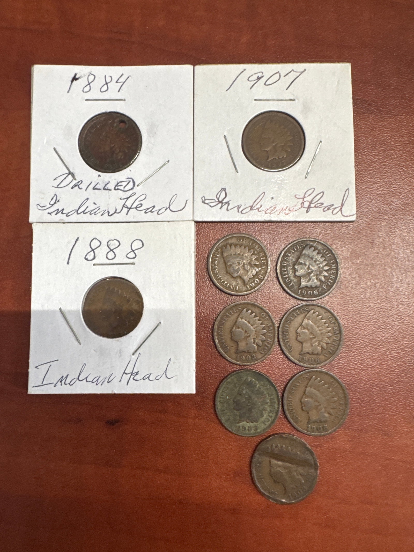 Collection of Indian Head Pennies: A collection of Indian Head pennies, including three housed in protective sleeves with handwritten dates (1884, 1907, 1888) and seven loose coins with dates ranging from 1903 to 1908.