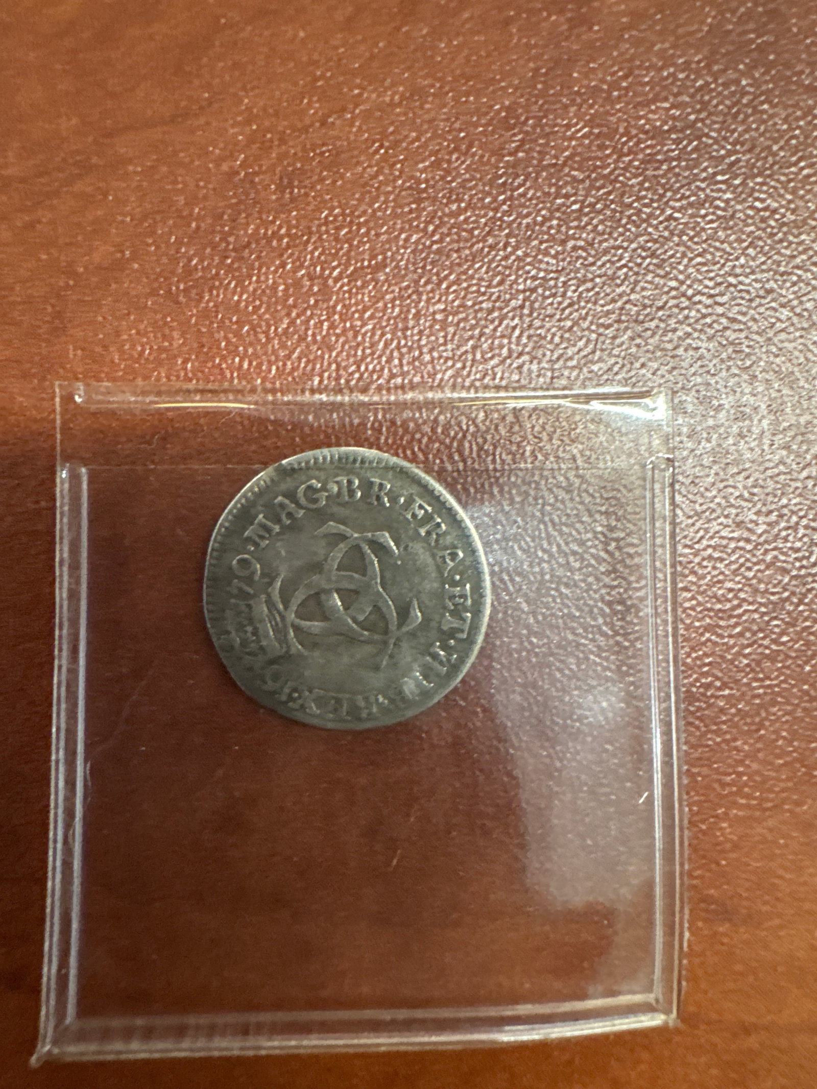 1679 England Silver Three Pence Coin of Charles II: A silver three pence coin from England, dated 1679. Features a portrait of Charles II on one side with the inscription 'CAROLUS II DEI GRATIA' and a triquetra symbol on the reverse. 