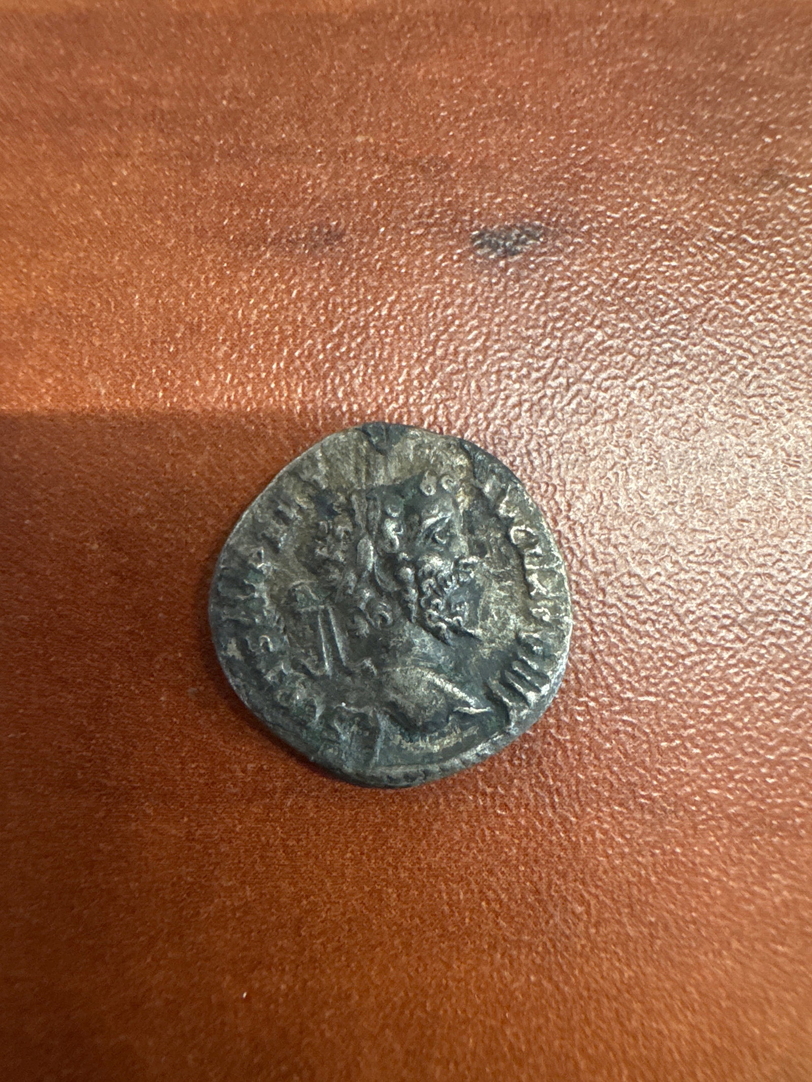 Ancient Roman Silver Coin: A silver coin from the Roman era, featuring a profile portrait on one side and a standing figure on the other. The details are worn but discernible, indicating its age and historical significance.