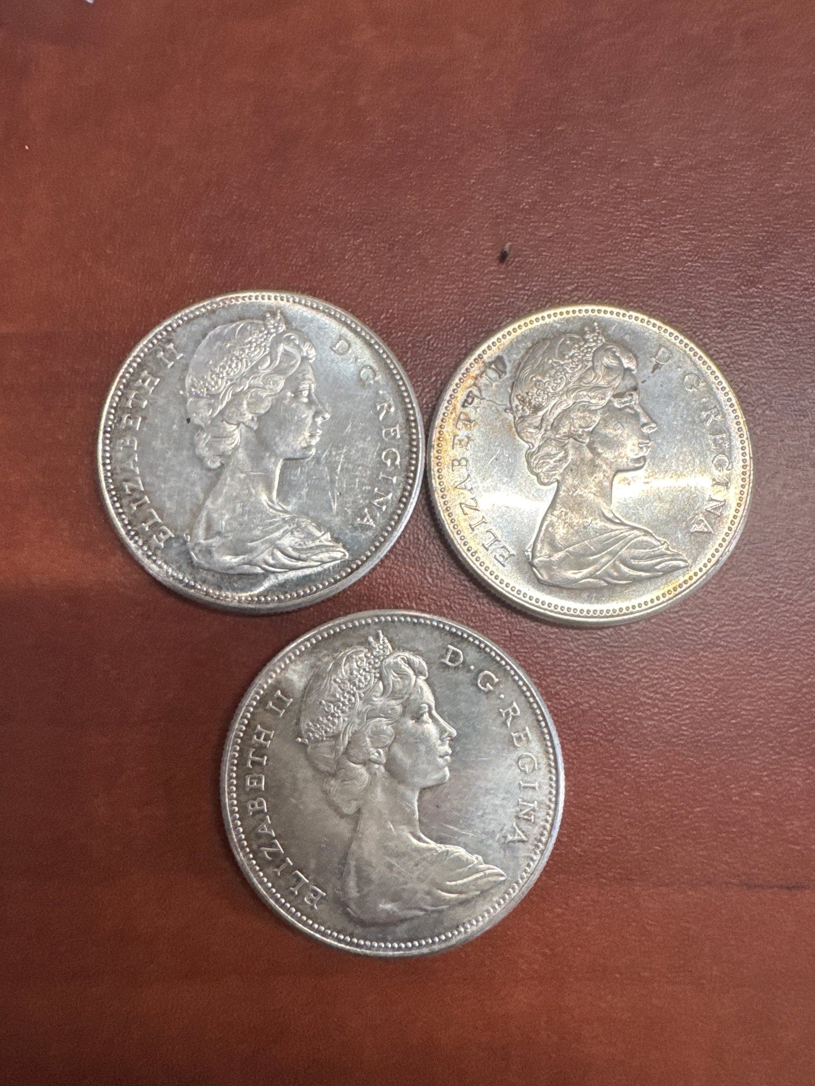 Three Canadian Silver Dollar Coins: A collection of three Canadian dollar coins, each featuring Queen Elizabeth II on the obverse and a Canada Goose in flight on the reverse. The coins are dated 1867-1967, commemorating Canada's cen