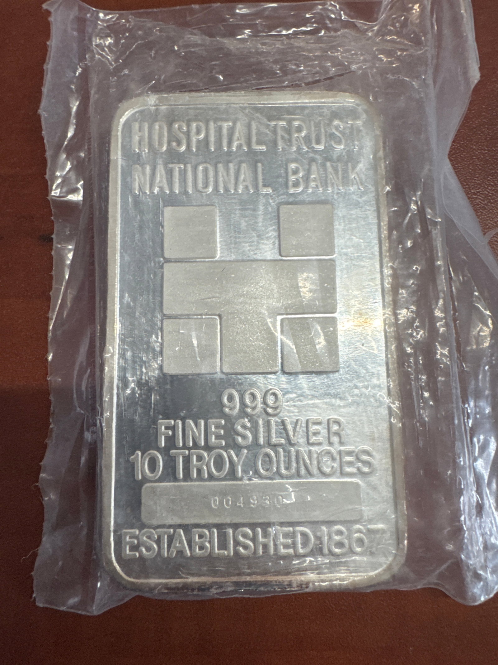 Hospital Trust National Bank 10 Troy Ounces 999 Fine Silver Bar: A 10 troy ounce bar of 999 fine silver from Hospital Trust National Bank, established in 1867. The obverse features the bank's logo and specifications, while the reverse has an intricate geometric
