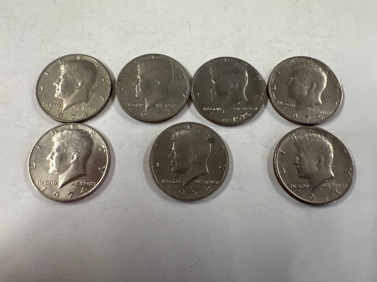 Collection of Seven Kennedy Half Dollar Coins: This lot features seven Kennedy half dollar coins. The obverse of each coin displays a profile of John F. Kennedy, while the reverse features the Presidential Seal. 