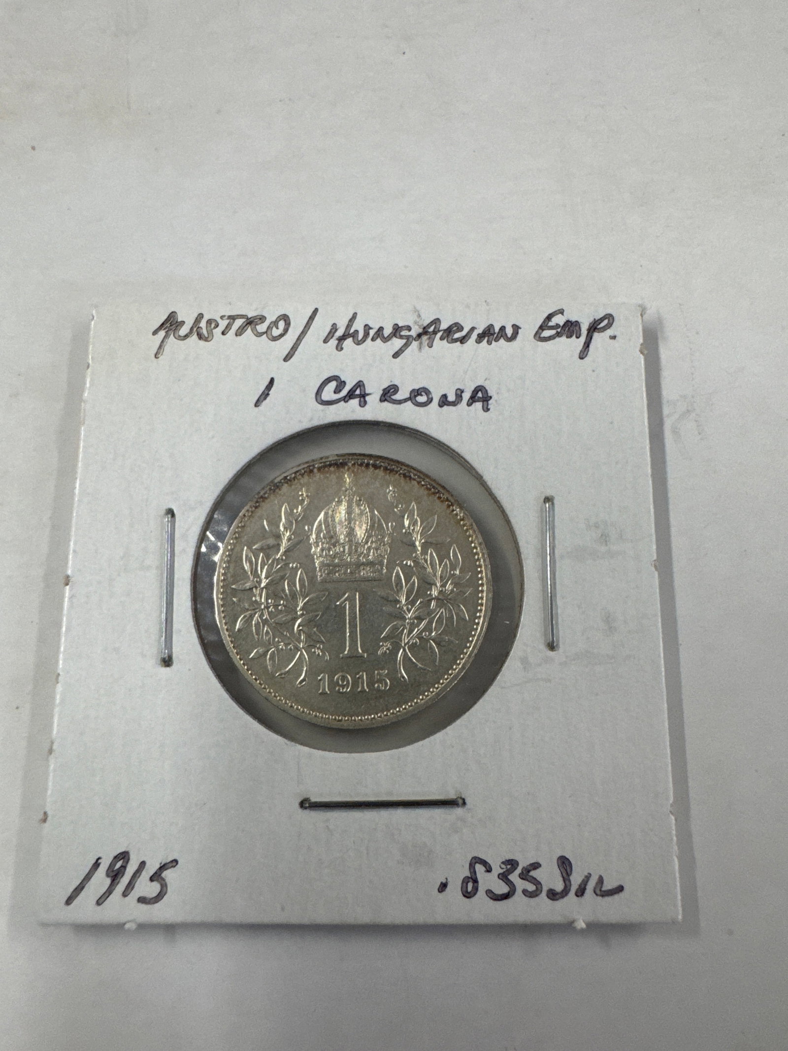 1915 Austro-Hungarian Empire 1 Corona Silver Coin: A silver 1 Corona coin from the Austro-Hungarian Empire, dated 1915. The obverse features a portrait of Emperor Franz Joseph I, and the reverse displays the imperial crown and denomination.