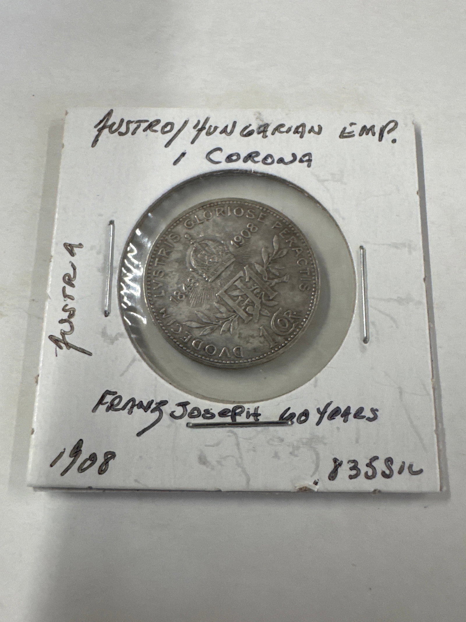 1908 Austro-Hungarian Empire Franz Joseph I 1 Corona Silver Coin: A silver 1 Corona coin from the Austro-Hungarian Empire, dated 1908. The obverse features a portrait of Emperor Franz Joseph I, and the reverse displays the imperial coat of arms. 
