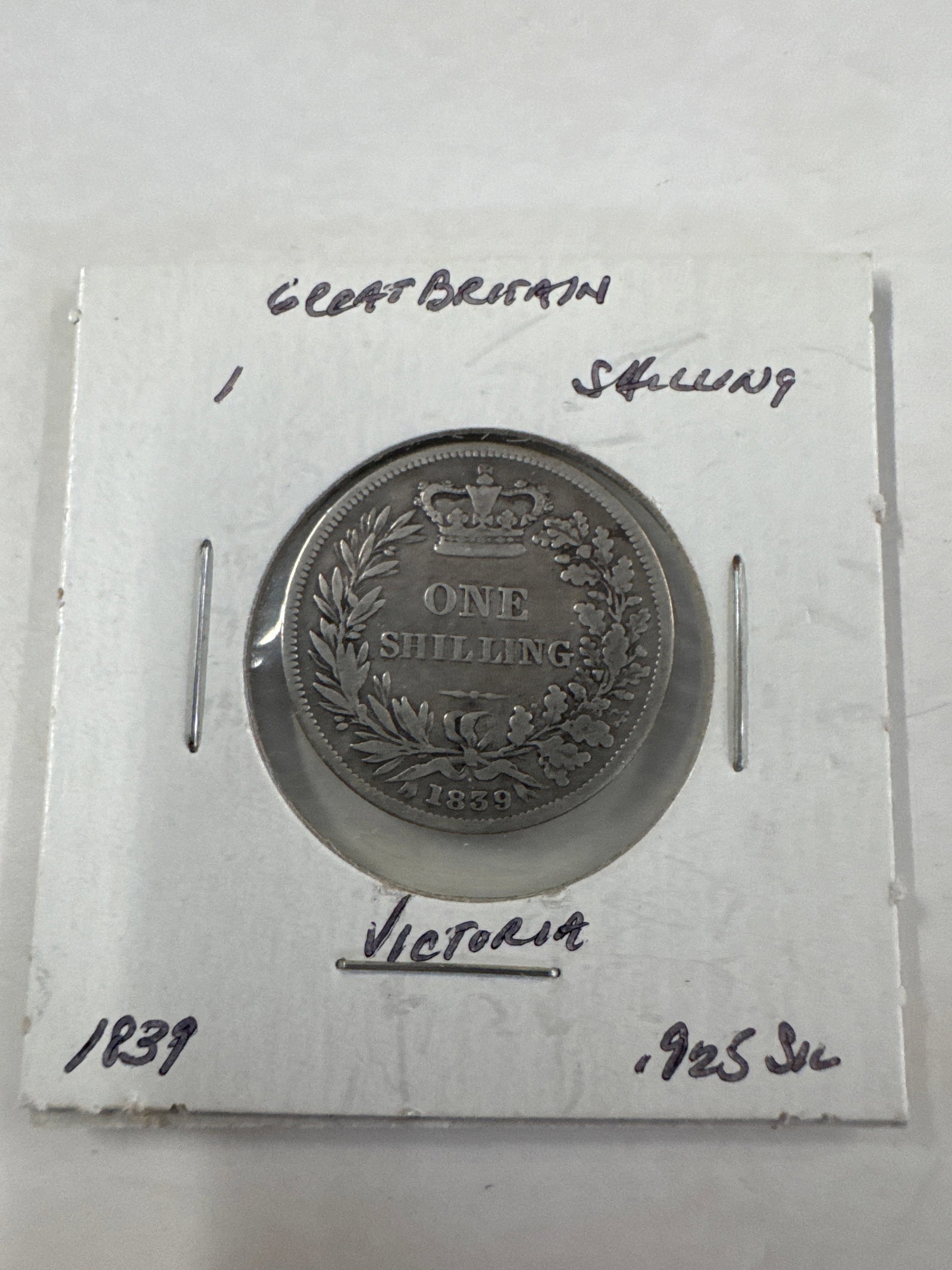 1839 Great Britain One Shilling Coin - Victoria: A silver coin from Great Britain, dated 1839, featuring Queen Victoria's profile on one side and the inscription 'ONE SHILLING' surrounded by a wreath on the other. The coin is .925