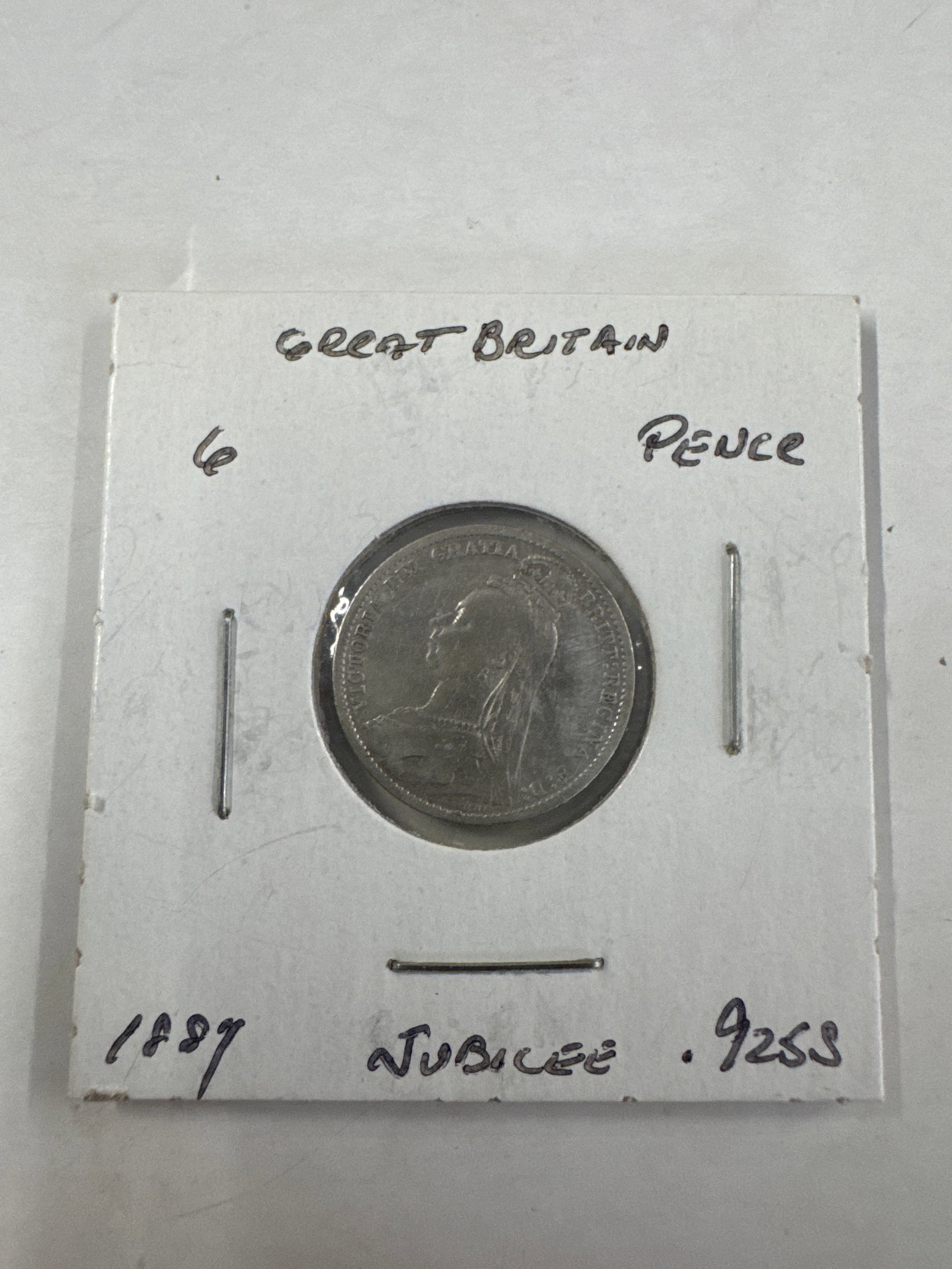 Great Britain 1887 Six Pence Jubilee Coin: A silver six pence coin from Great Britain, dated 1887, featuring Queen Victoria's Jubilee portrait on the obverse and the royal crown and denomination on the reverse. The coin is housed in a prot