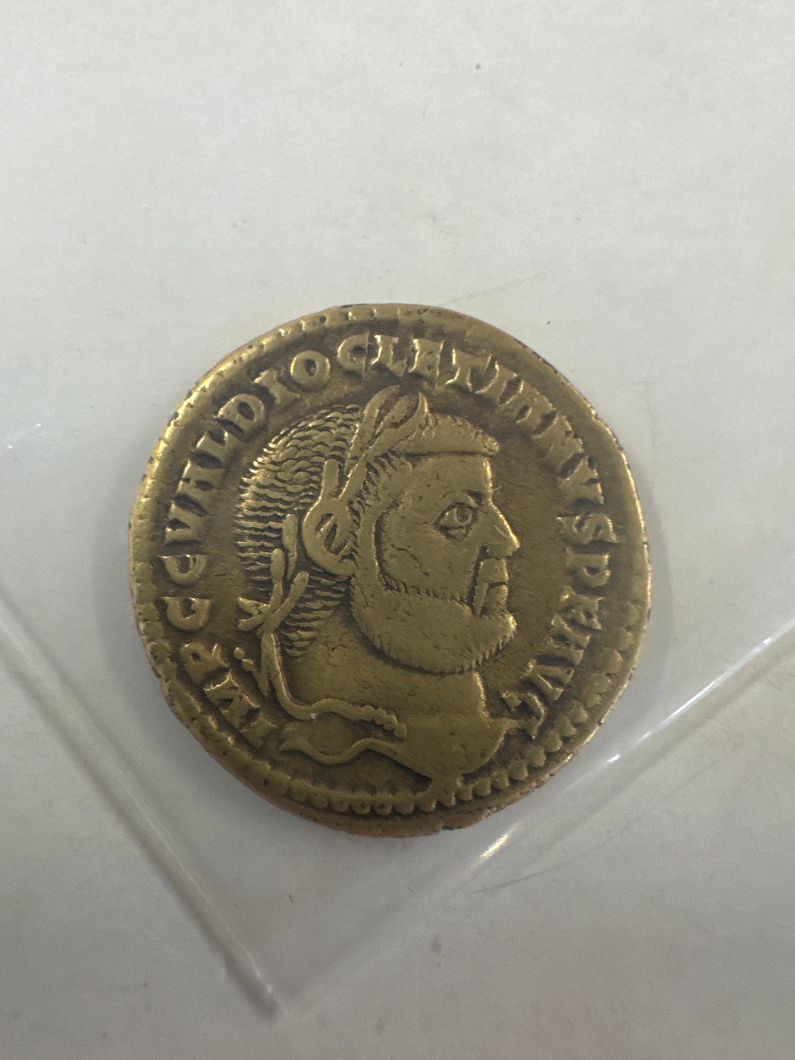 Replica Ancient Roman Coin with Emperor Portrait and Standing Figure: This brass Roman coin replica features an emperor's profile portrait on the obverse and a standing figure on the reverse, both surrounded by Latin inscriptions. The coin exhibits wear consistent w