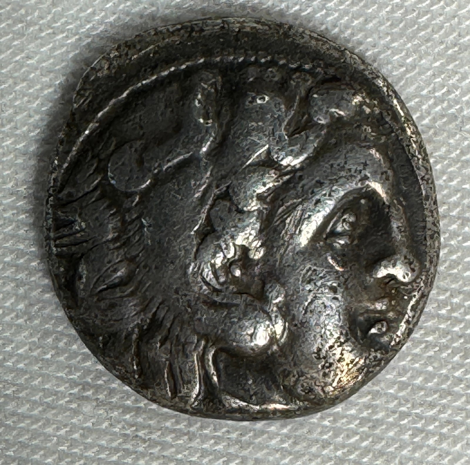 Ancient Silver Coin with Seated Figure: Ancient silver coin, approximately 1.6 cm in diameter.