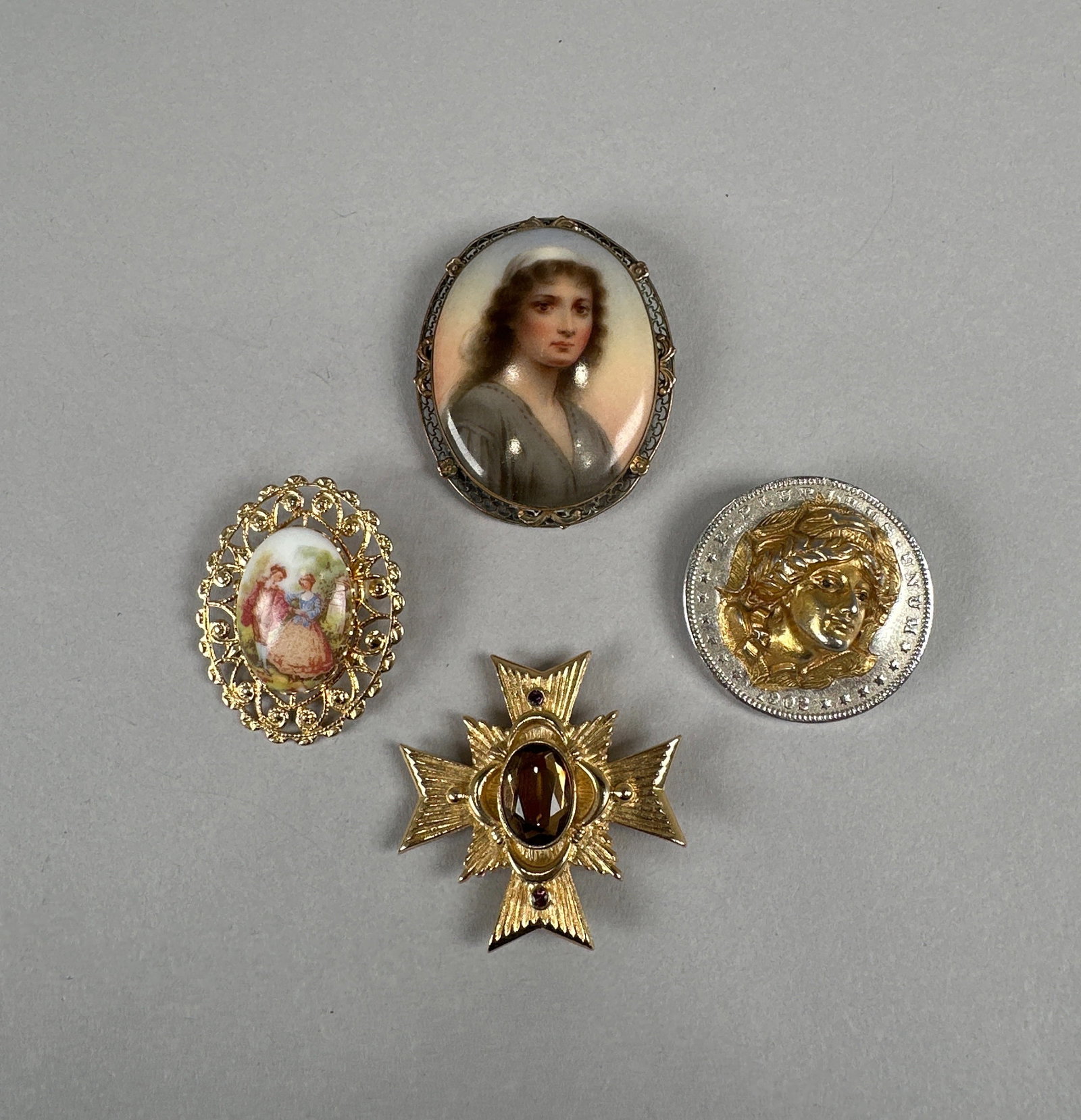 Collection of Four Brooches: This collection features four distinct brooches. One is a portrait miniature of a woman in an oval frame with intricate metalwork. Another is a gold-tone cross brooch with a central oval garnet. A thi