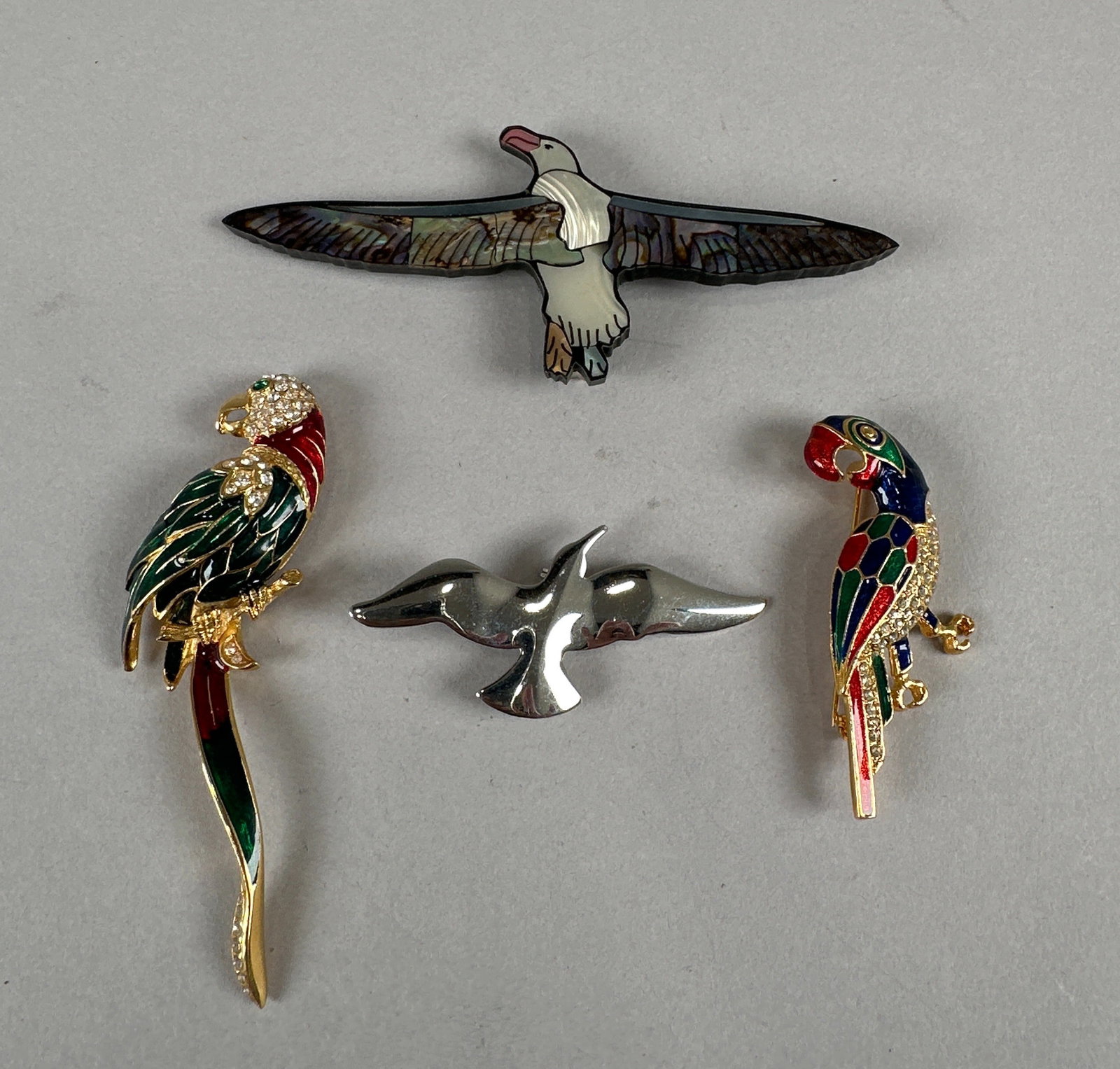 Four Bird Pins/Brooches: A collection of four unique bird-themed brooches. Features two colorful enamel and rhinestone parrots, a sleek silver-tone seagull, and an eagle brooch with abalone shell inlay. Weight: 46g. Dimension