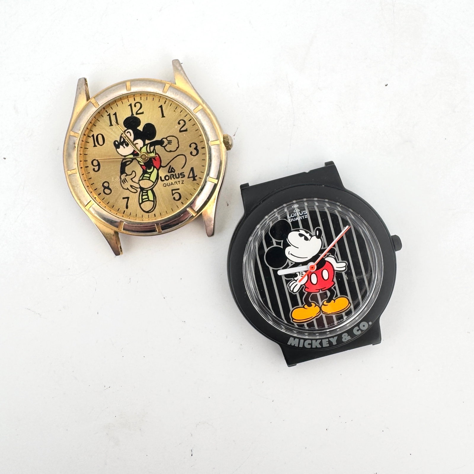 Two Lorus Quartz Mickey Mouse Wristwatches: A pair of Lorus Quartz wristwatches featuring the iconic Mickey Mouse. One watch has a gold-tone case with Arabic numerals and a depiction of Mickey Mouse in motion. The second watch has a black case 