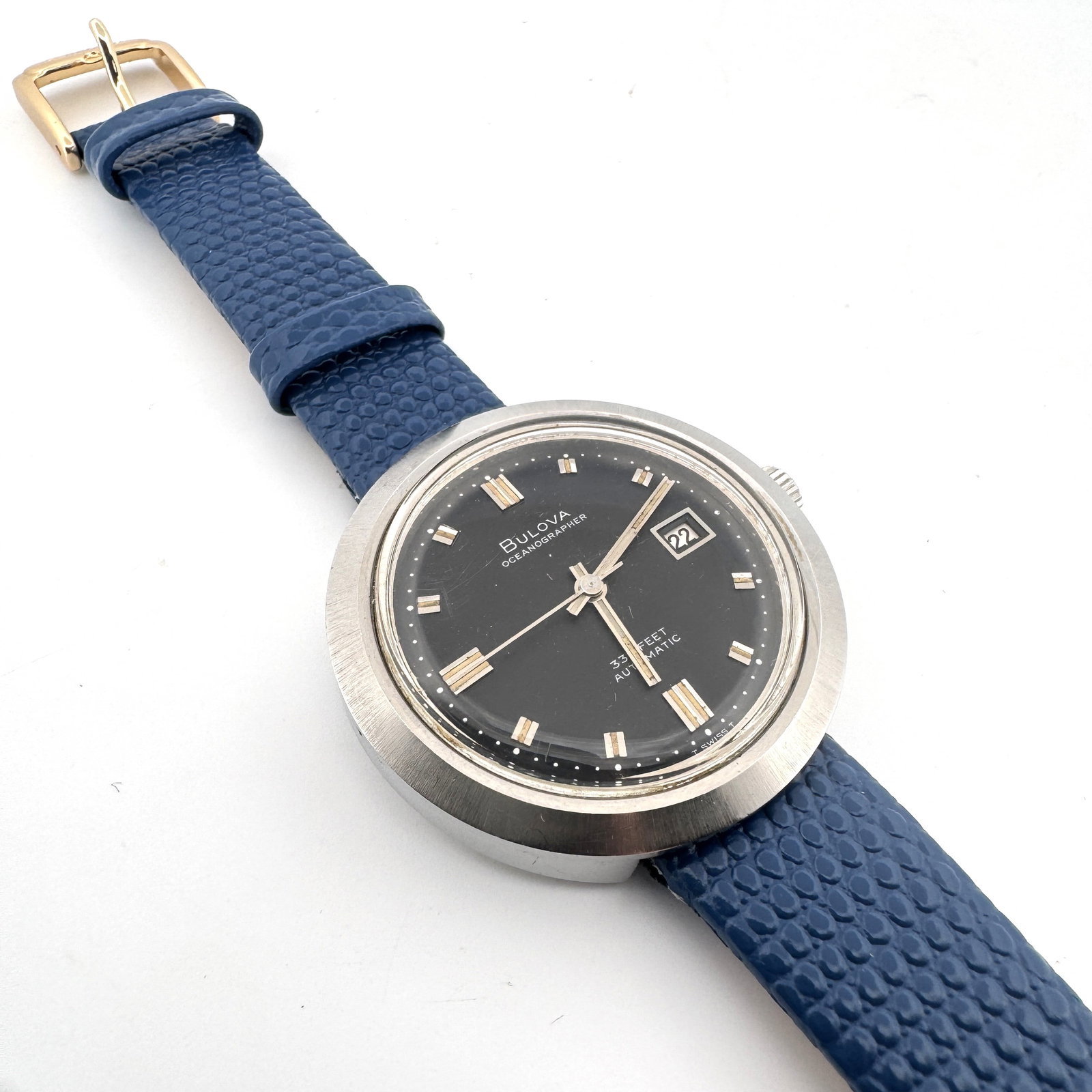 Vintage Bulova Oceanographer Automatic Watch: A vintage Bulova Oceanographer automatic watch with a black dial and date complication. The watch features a stainless steel case and a blue textured leather strap. Dimensions: 8.5''. 