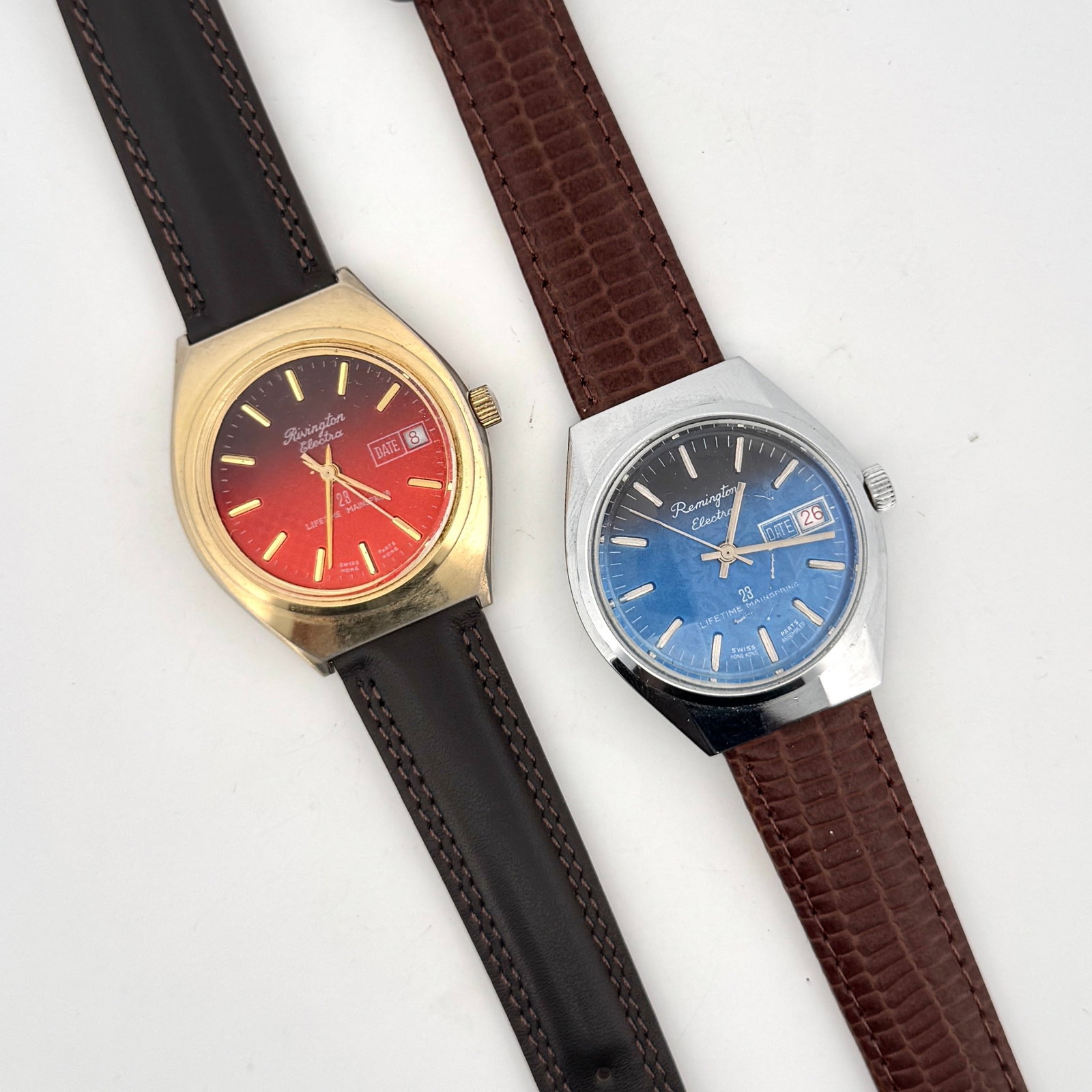 Two Remington Electra Wristwatches: A pair of vintage Remington Electra wristwatches. One features a red gradient dial with gold-tone case and black leather strap. The other has a blue dial with a silver-tone case and brown textured lea