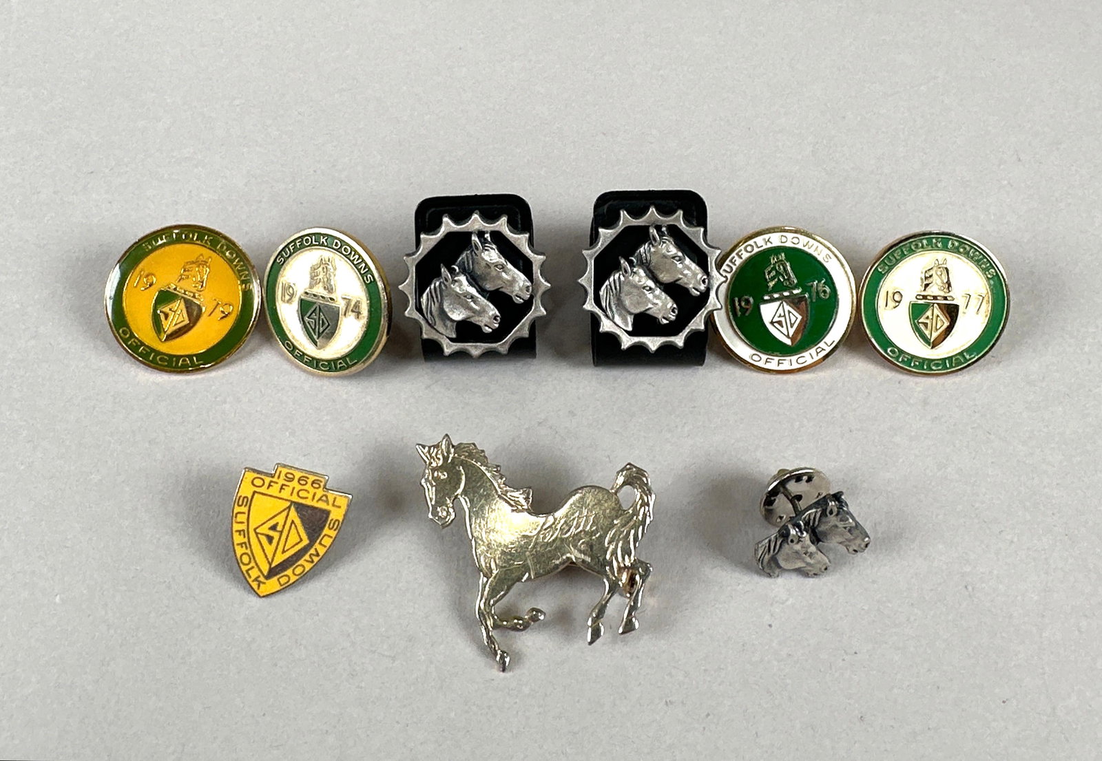 Collection of Horse-Themed Pins and Cufflinks: This lot features a collection of horse-themed items, including several enamel pins with equestrian motifs and dates. It also includes a pair of cufflinks with horse heads, a silver-toned horse brooch