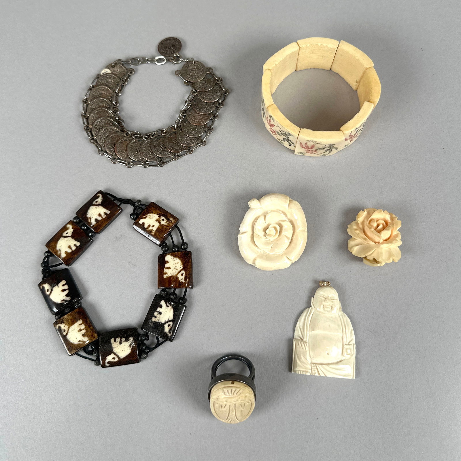 Collection of Bracelets, Charms, and Carvings: This collection features a variety of decorative items including a coin bracelet, an ivory-toned bracelet with floral motifs, a dark wood bracelet with carved elephants, a carved ivory Buddha charm, a