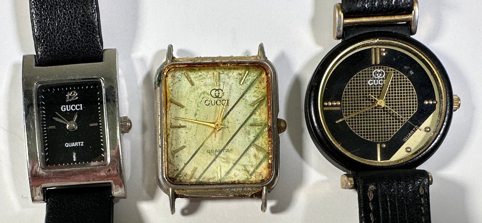 Three Gucci Quartz Wristwatches: Three Gucci quartz wristwatches with black leather straps. One with a square silver-tone case and silver dial, one with a square gold-tone case and gold dial (without band), and one with a r