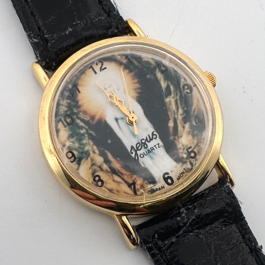 Jesus Quartz Wristwatch with Image on Dial: Jesus Quartz wristwatch featuring an image on the dial. Gold-tone case with a black leather strap. Weight: 0.8oz. Size: 8.75'' long