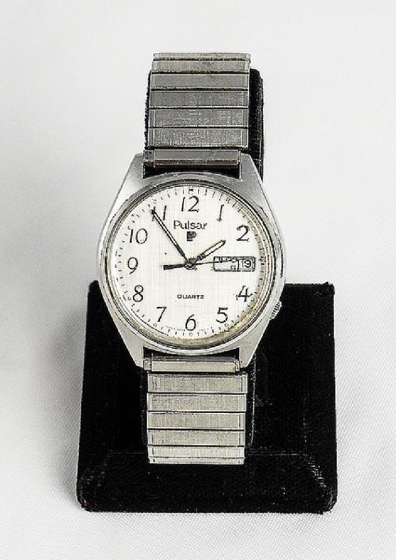 Vintage 1980's Men's Pulsar Quartz Fashion Watch: Men's Pulsar brand with stainless steel stretch band. Light silver colored face with black numbers & dials. Day & date on right side of face. Water resistant. Used condition, with light scratches to f
