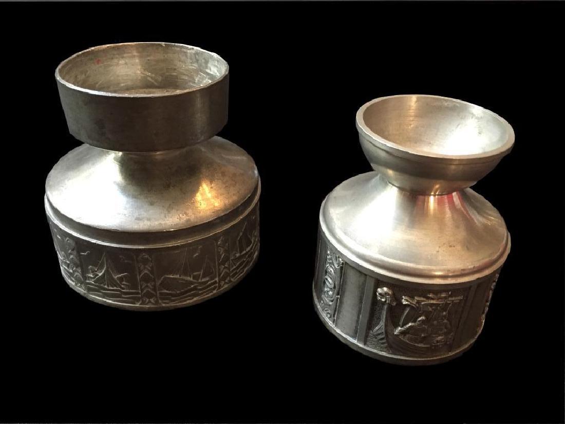 Pair of Norwegian Pewter Viking Candlesticks: Pair of Norwegian pewter candlestick candle holders. Smaller holder is Konge Tinn, stamped "KONGE TINN, HS, NORWAY on inside. Depicts scenes of Vikings ready for battle & in ships 3" H X 2 1/2'D. Larg