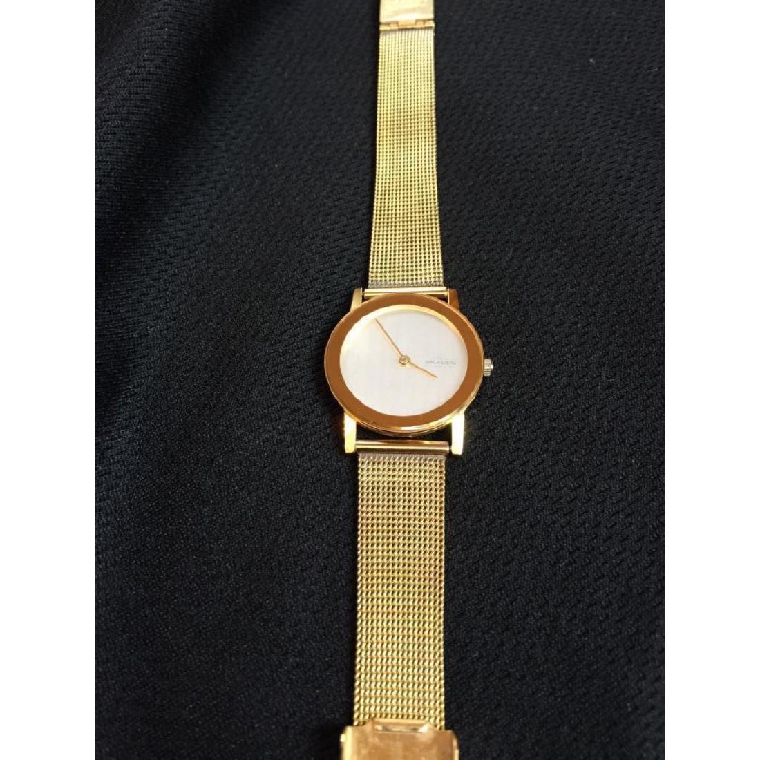 Ladies Contemporary Gold Skagen Watch: Skagen Denmark 39SGG Ultra Slim. Japan quartz movement. Stainless steel gold mesh band. White face with gold hands. Modern styling. In very good condition. Needs replacement battery.