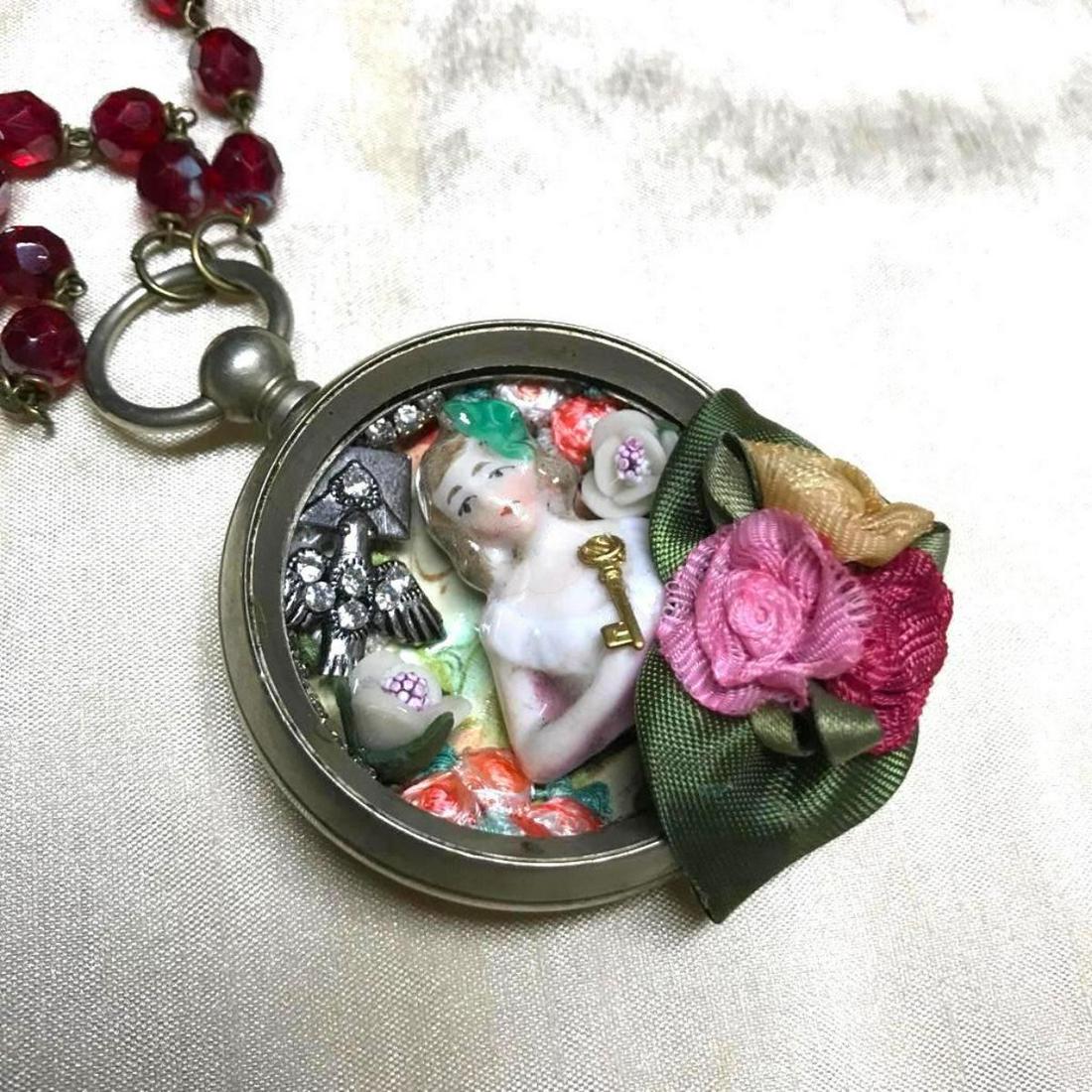 Vintage Pocket Watch Artisan Doll Necklace: Vintage early 20th-century pocket watch, combined with an Art Deco era broken porcelain doll & ribbon work, re-created into a one of a kind artisan created pendant, with vintage ruby Czech glass beads