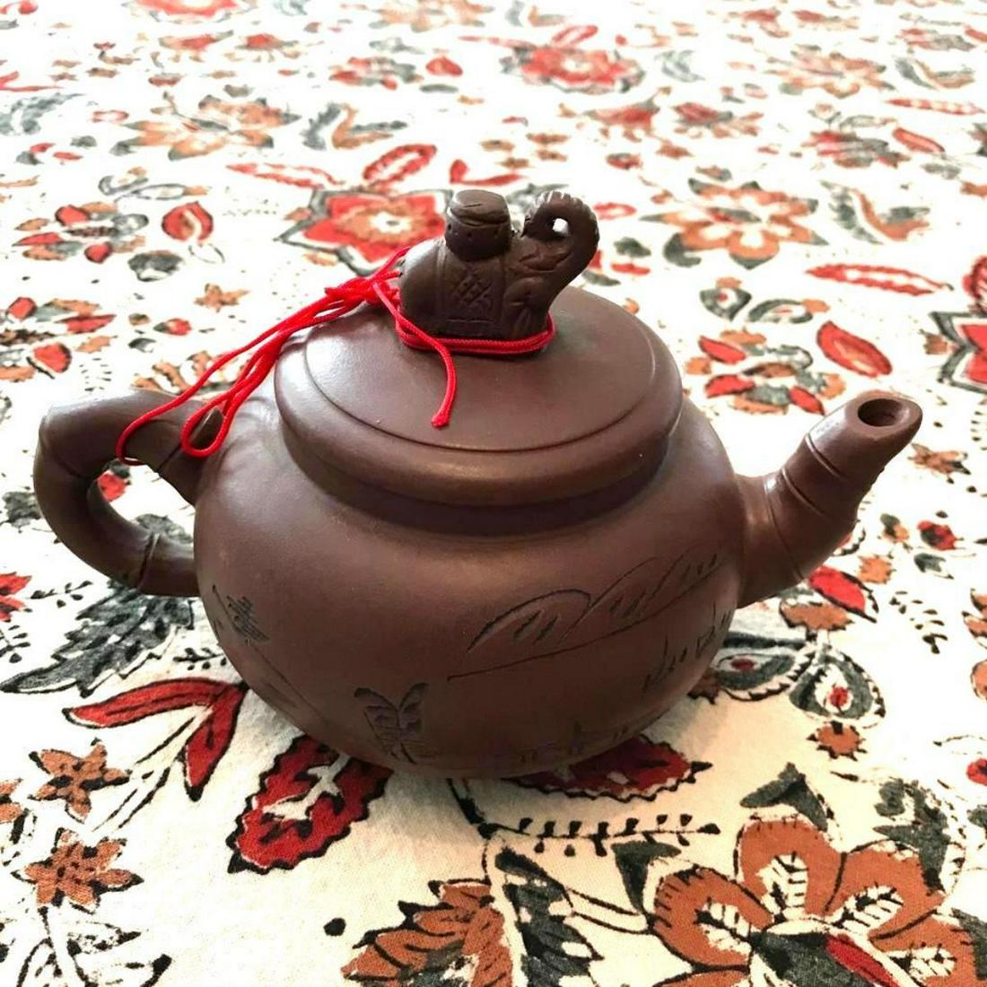 Japanese Yixing Clay Teapot, Elephant: Japanese purple yixing clay teapot, with bamboo design handle & spout, elephant on top of lid. Characters, letters around one side of the teapot & on the other, & landscape scene, a house with mountai