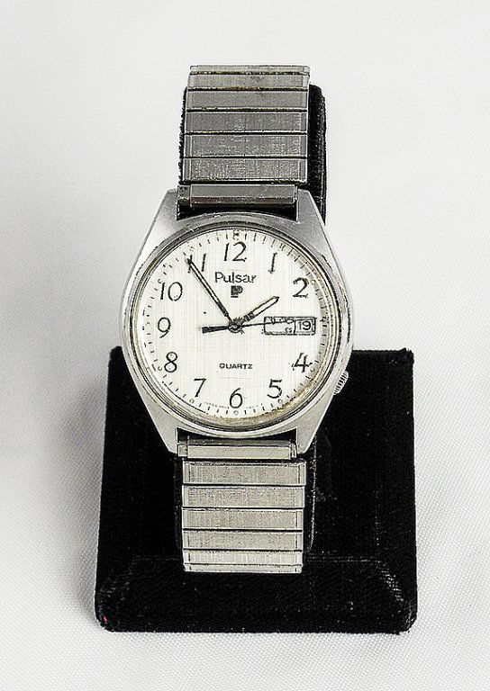 Vintage 1980's Men's Pulsar Quartz Fashion Watch: Men's Pulsar brand with Stainless Steel stretch band. Light silver colored face with black numbers & dials. Day & Date on right side of face. Water resistant. Used condition, with light scratches to f