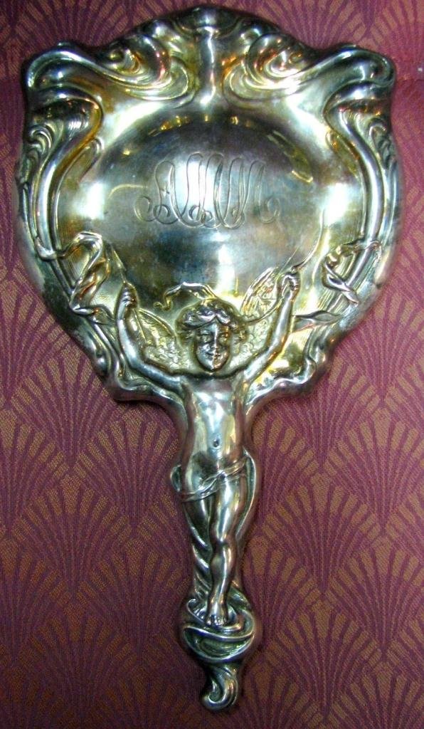 Late 19th Century Vanity Mirror: Victorian, Silver-plate vanity mirror. Handle features a cupid with bow & arrow. Monogrammed. Round, beveled glass is in good condition. 10" long. 5 1/2" at widest area. Gorgeous piece for an antique