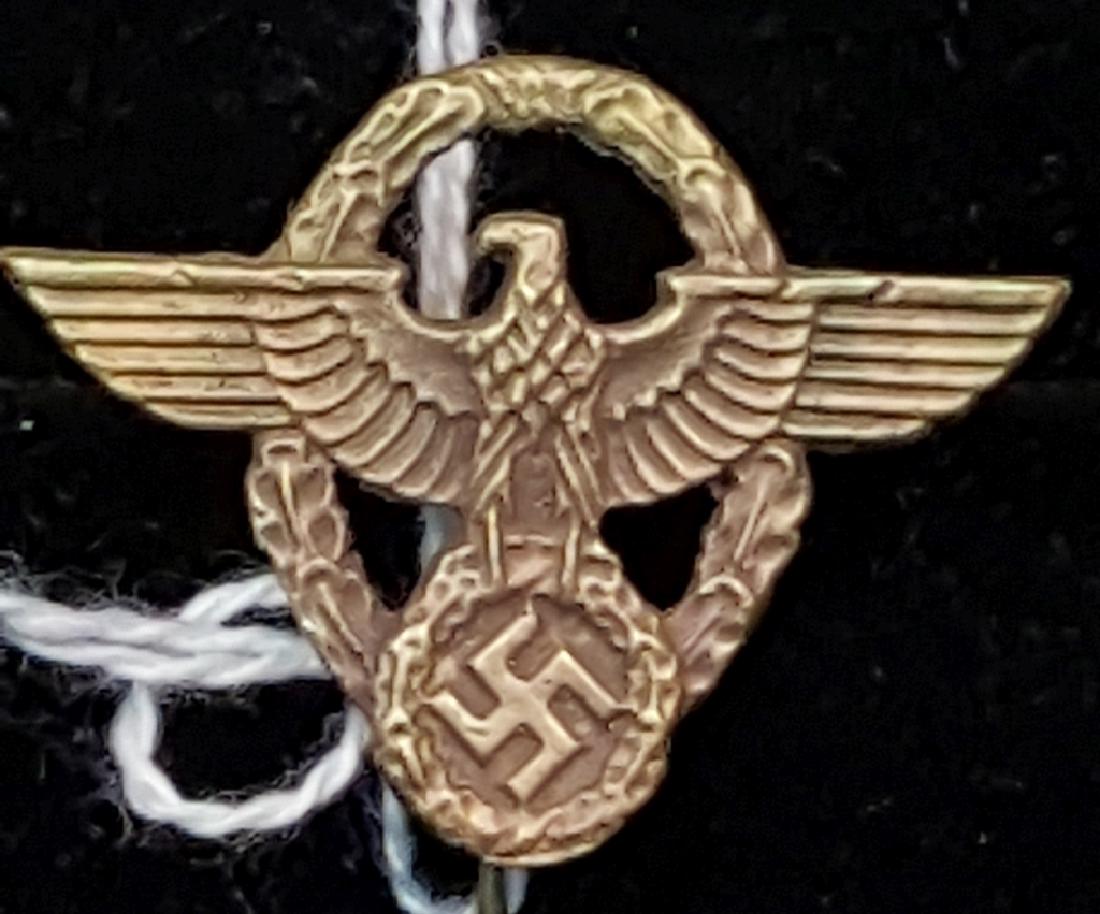 Gold Police Cap Eagle German WWII Stick Pin: This Gold Police Cap Eagle features a closed wreath of oak leaves and a superimposed open-winged eagle. The eagle grasps a wreath and raised mobile swastika. Part of a 44 Piece GERMAN WWII COMBAT AND 