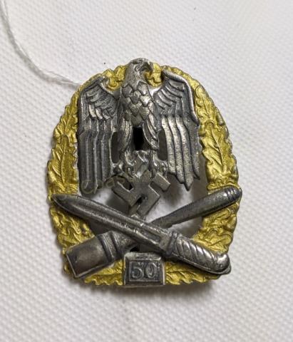 WWII German 3rd Reich Assault Badge 50 Engagements: WWII German assault badge for 50 engagements. Badge features an iron eagle over a K98 bayonet and a grenade. Gold wreath with silver Eagle, Swastika and weapons.