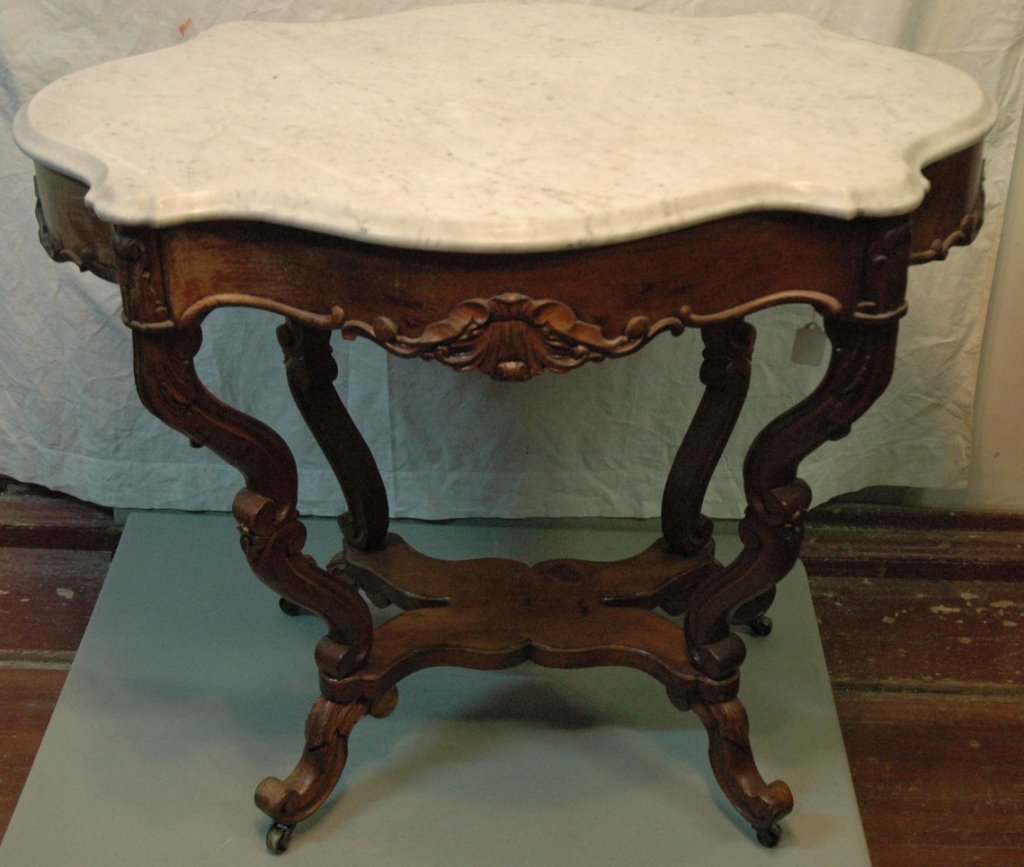 A Victorian Walnut marble top table: The table with a carved skirt, with a white marble turtle top, the top with minor damage to one edge, 29" tall x 35" wide by 25.5" deep.
